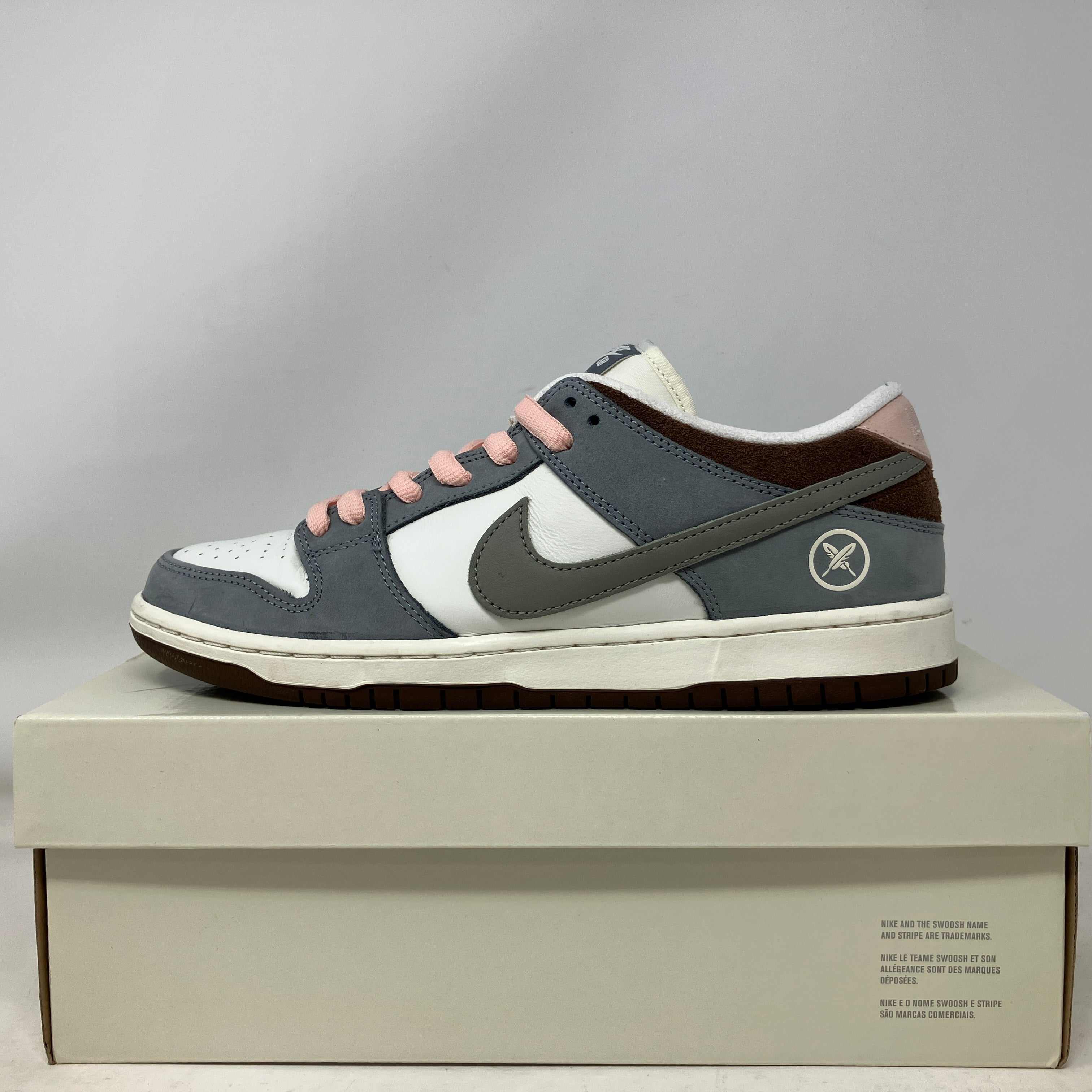 Nike SB Dunk Low sneaker in grey, white, and pink on a beige shoebox, showcasing street style and skate culture design