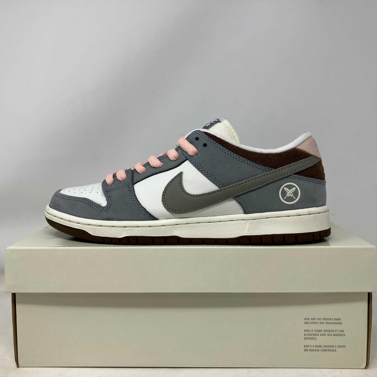 Nike SB Dunks low-top sneaker in grey and cream leather, with pink laces, dark brown panels and side swoosh emblem.