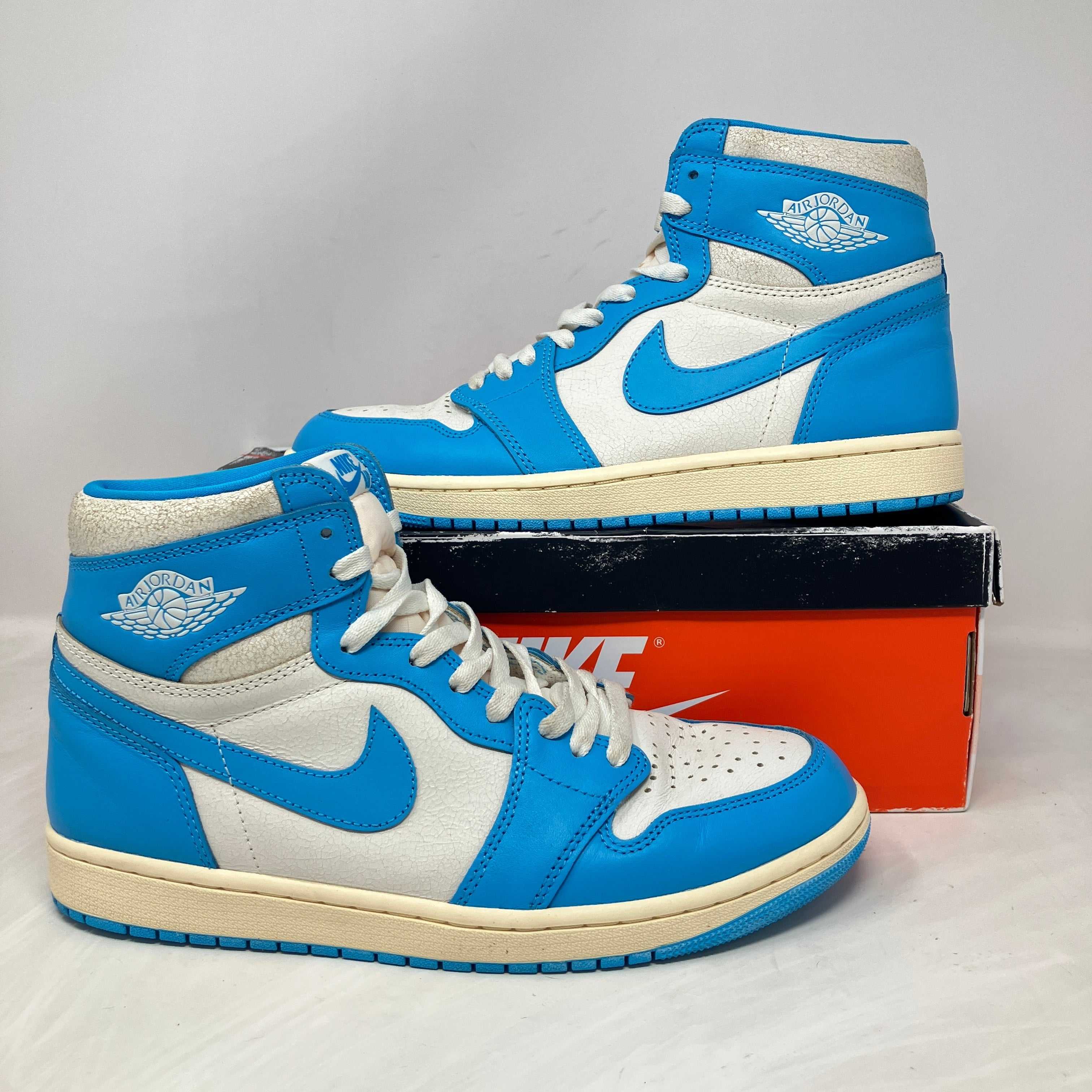 Pair of blue and white Air Jordan 1 sneakers displayed on and beside an orange Nike shoebox highlighting sneaker price trends