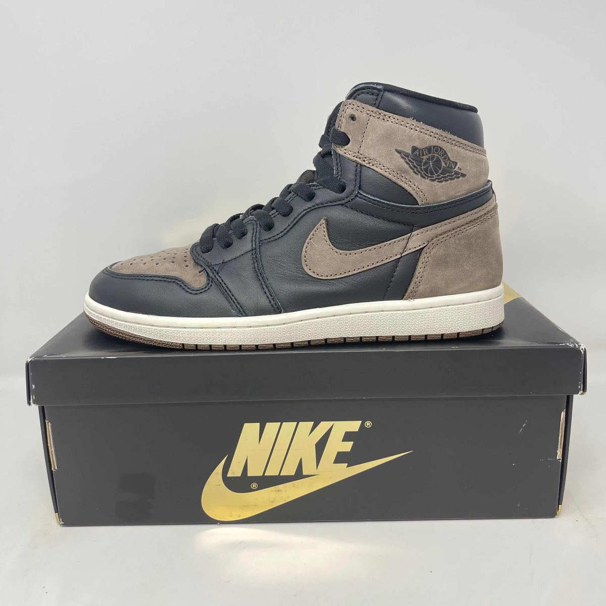 Air Jordan 1 high-top sneaker in charcoal leather and taupe suede, with a cream sole and Wings logo; Hidden Realm Sneaker Shop.
