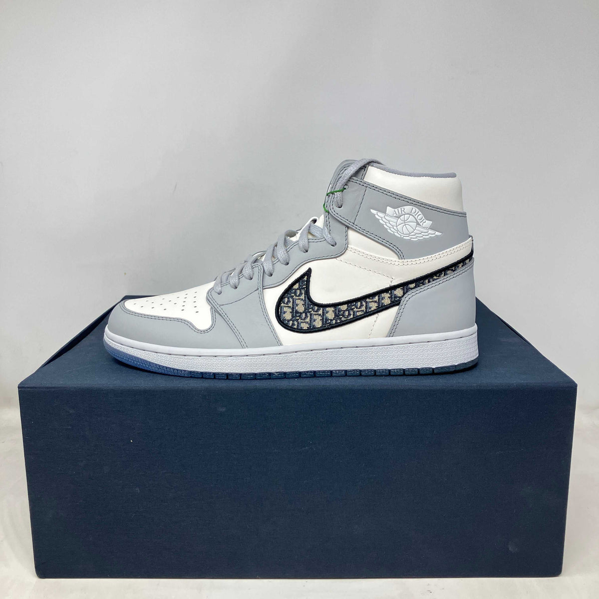 Jordan 1 Retro High Dior sneaker in white and light grey leather with distinctive Dior monogram pattern on the Nike swoosh.