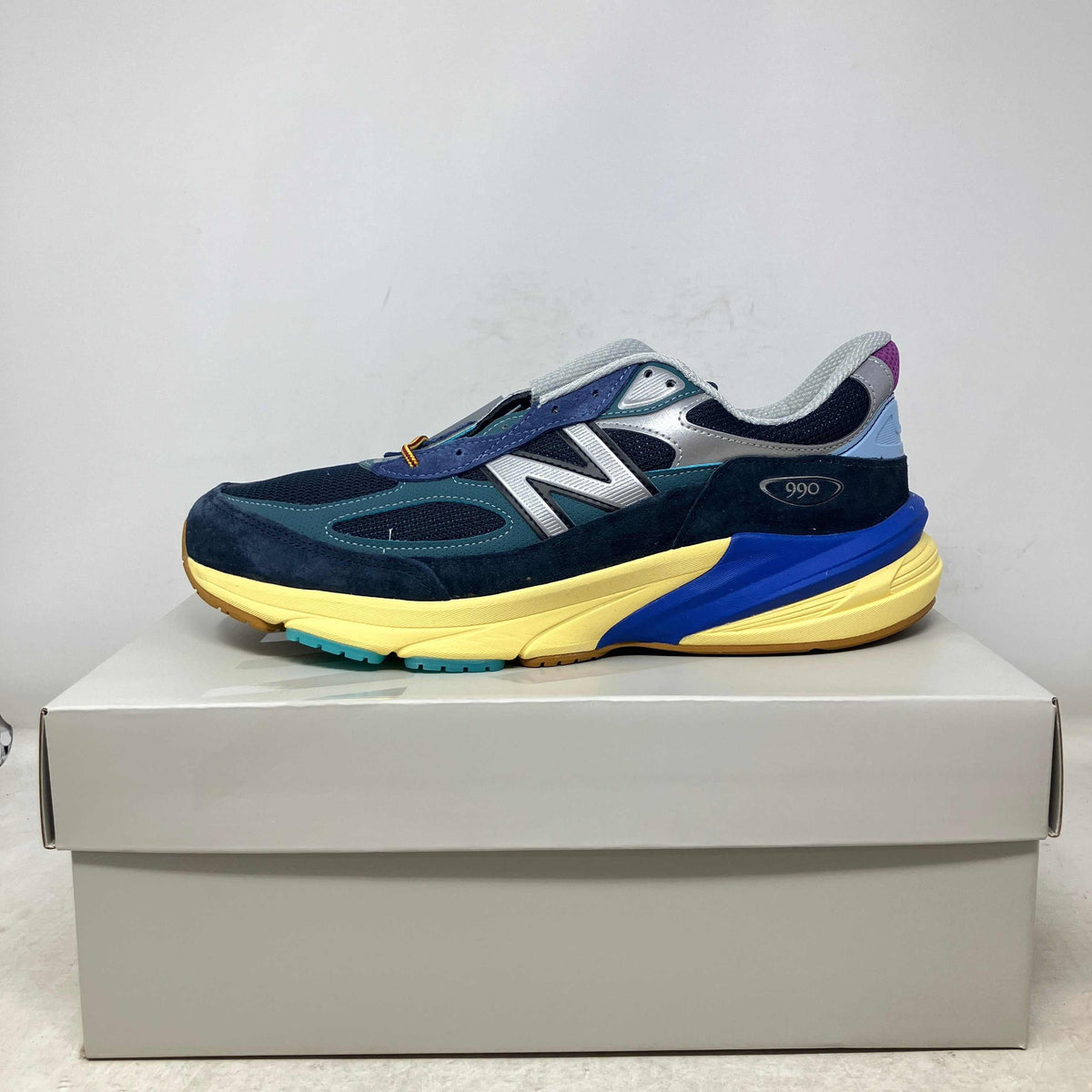 New Balance 990v6 sneaker in blue and teal suede with grey mesh, yellow sole, and blue accents on the midsole