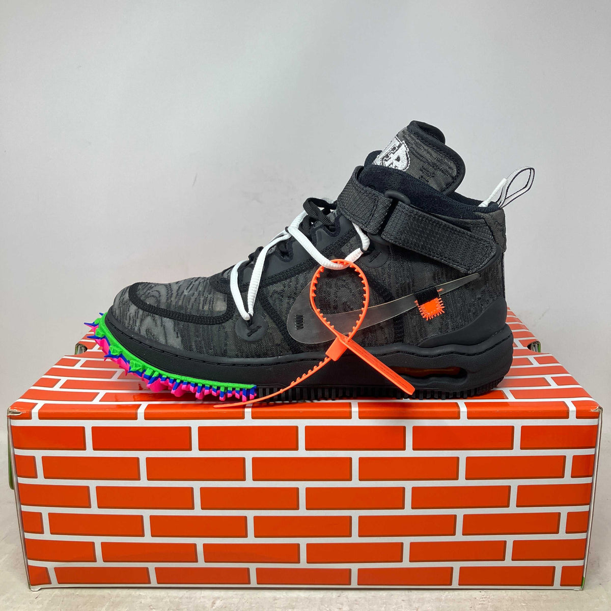 Nike Air Force 1 Mid black high-top sneaker with gray patterns, multicolor spikes on the sole, and an orange zip tie accessory.