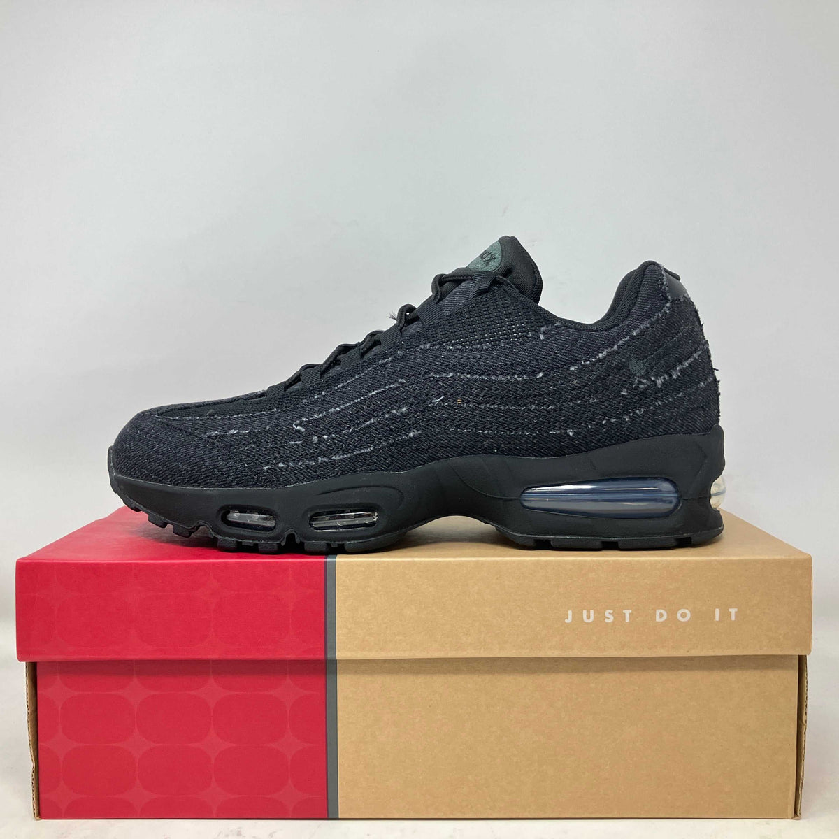Black Nike Air Max 95 sneaker with textured fabric upper and air cushion sole on a red and tan "Just Do It" box