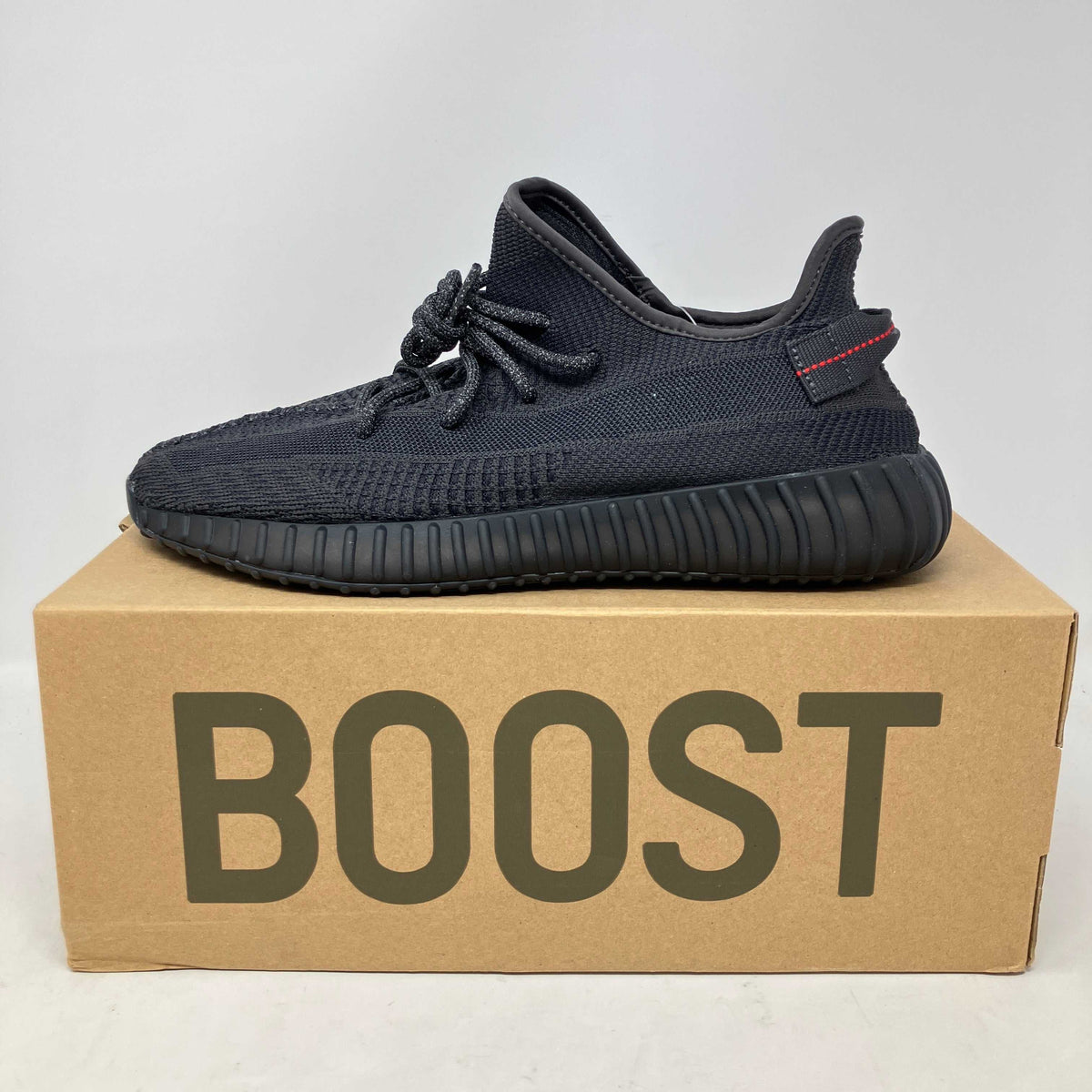 adidas Yeezy Boost 350 V2 black knit sneaker with ribbed sole and red accent on heel tab, non-reflective design