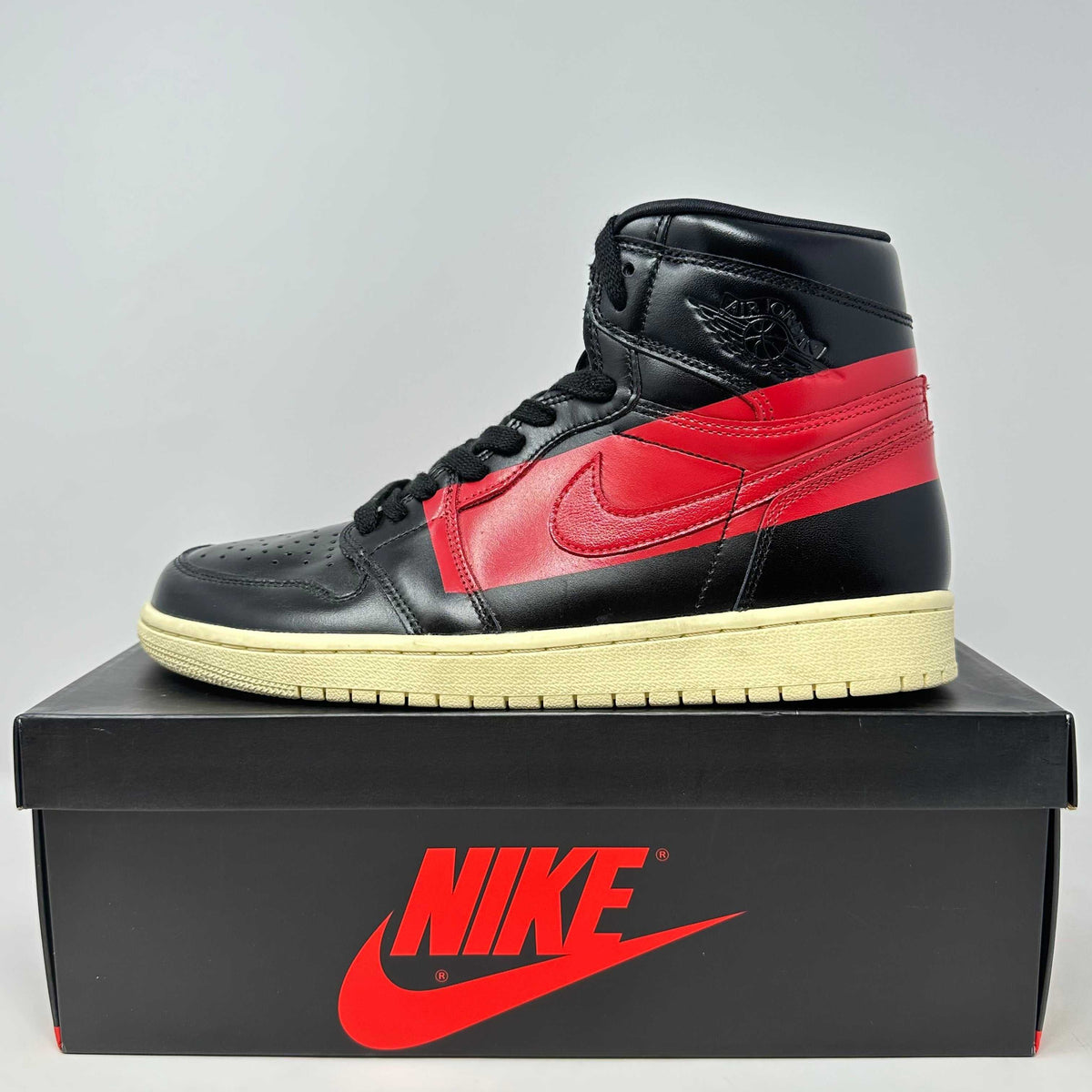 Jordan 1 Retro High OG black and red leather high-top sneaker with cream sole and Nike box in the background.