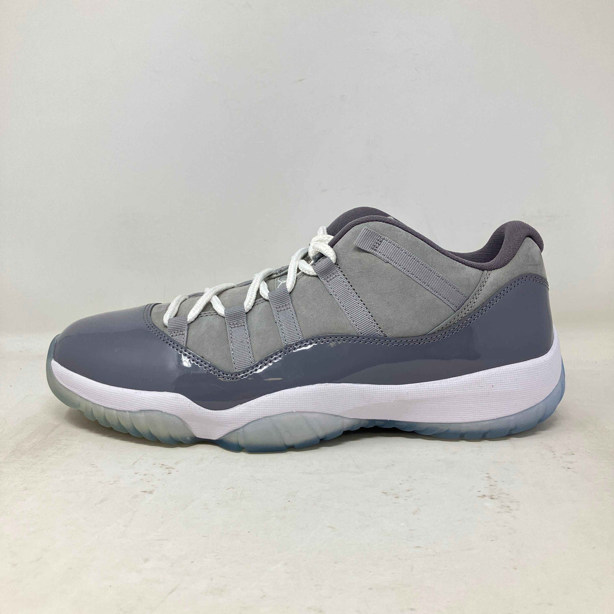 Jordan 11 Retro Low sneaker in cool grey with patent leather, suede, white laces, and translucent sole detailing.