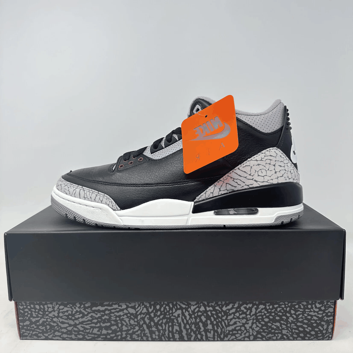 Jordan 3 Retro OG sneaker in black leather with grey elephant-print overlays, white midsole, and orange hang tag.