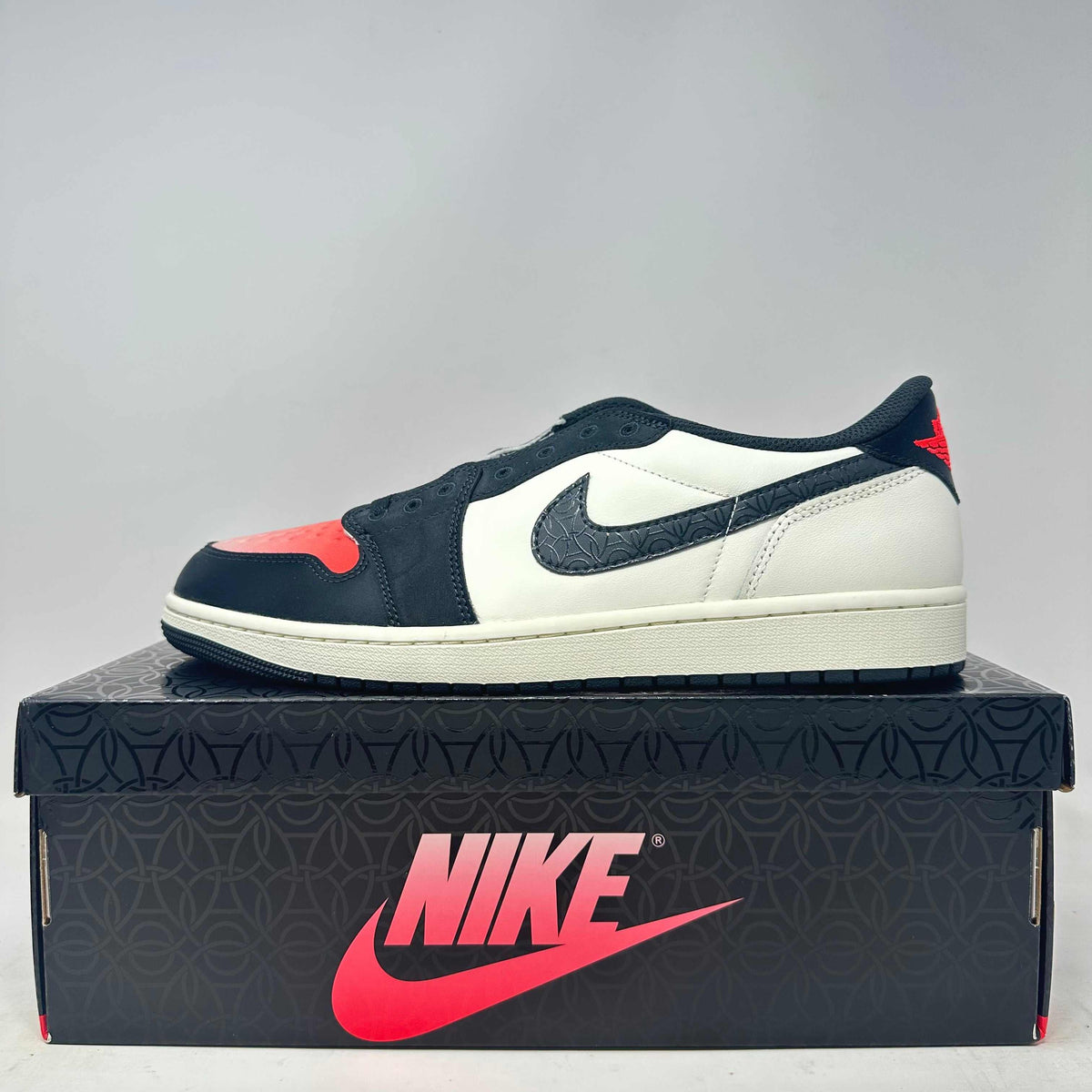 Jordan 1 Retro Low OG PSG sneaker in black, white, and red leather with textured Nike swoosh and red heel logo on a black Nike box.
