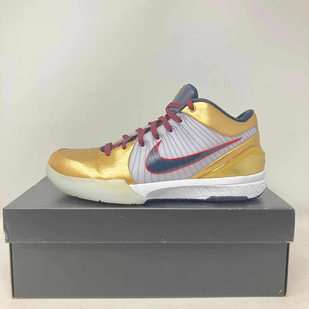 Nike Kobe 4 Protro basketball shoe in gold, grey, and red with a white sole and mesh upper detailing