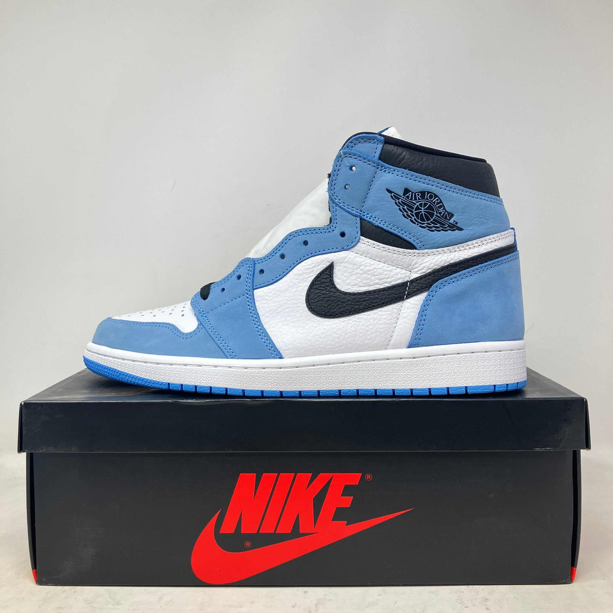 Jordan 1 Retro High OG sneaker in blue suede and white leather with black detailing and Nike logo on a black box with red text