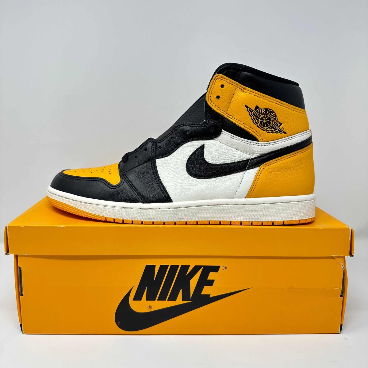 Jordan 1 Retro High OG Taxi sneaker in yellow, black, and white leather with the Nike swoosh and Air Jordan wings logo on the collar
