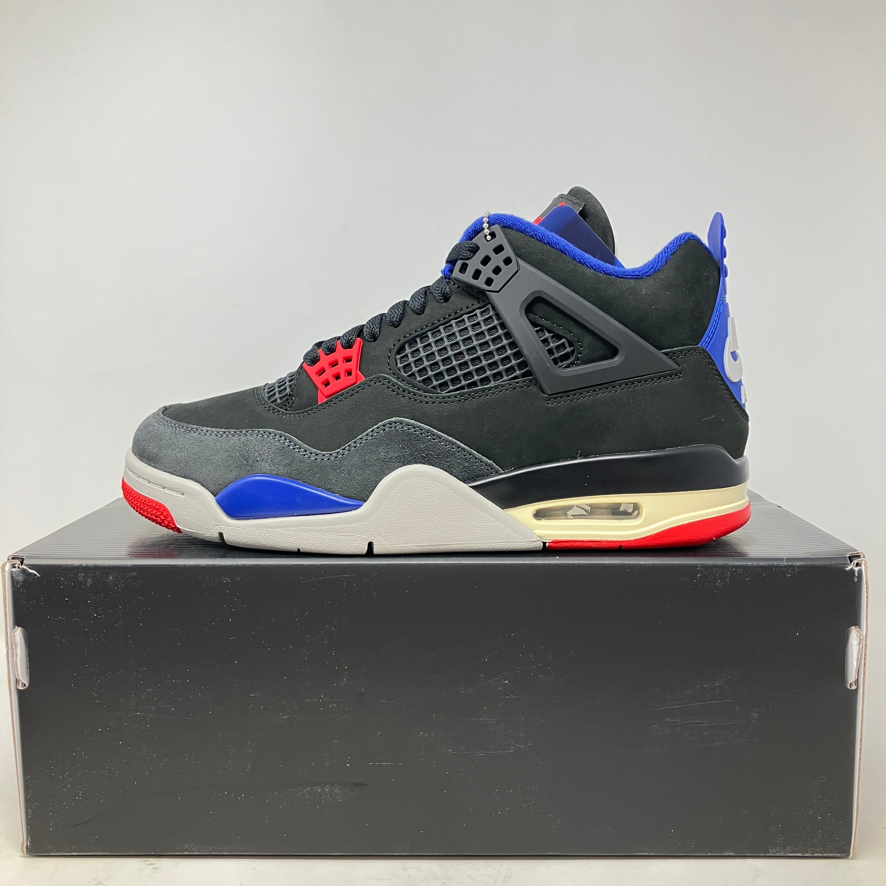 Jordan 4 Retro Rare Air sneaker in black with red, blue, and gold detailing, brand new on black shoebox