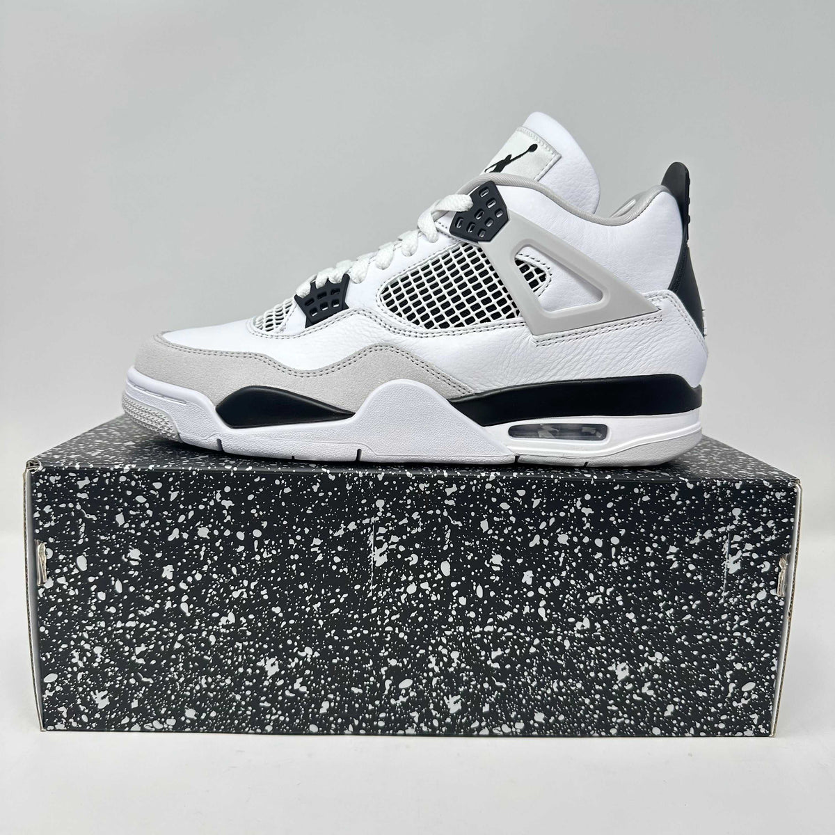 Jordan 4 Retro sneaker in white, black, and grey with mesh panels and a speckled black and white shoebox beneath.