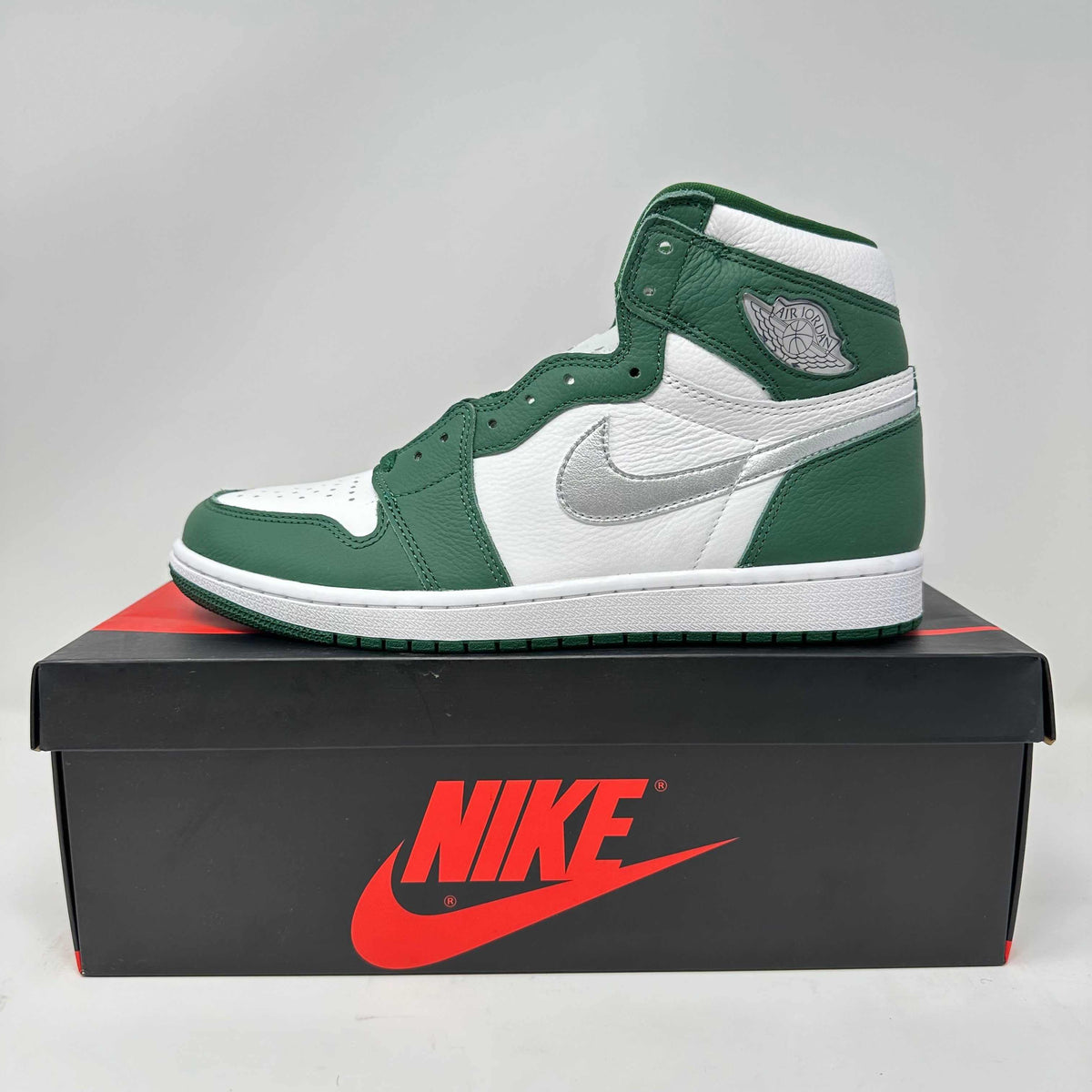 Jordan 1 Retro High OG sneaker in gorge green and white leather with a silver swoosh and high-top design on a black Nike box.