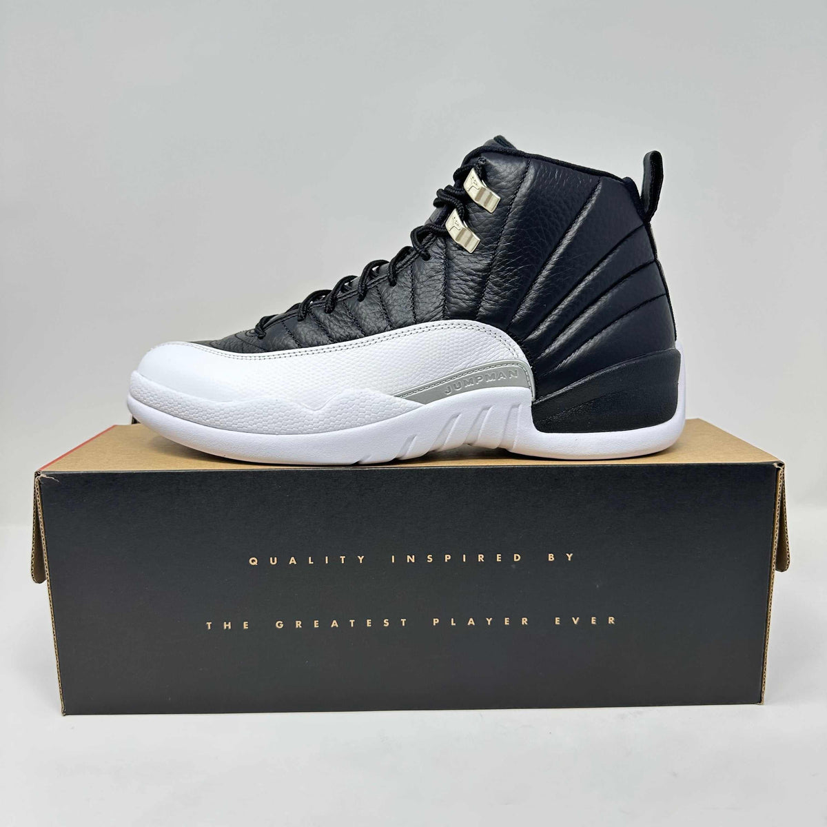 Jordan 12 Retro Playoffs high-top sneaker in black and white leather, with gold lace eyelets and sculpted sole.