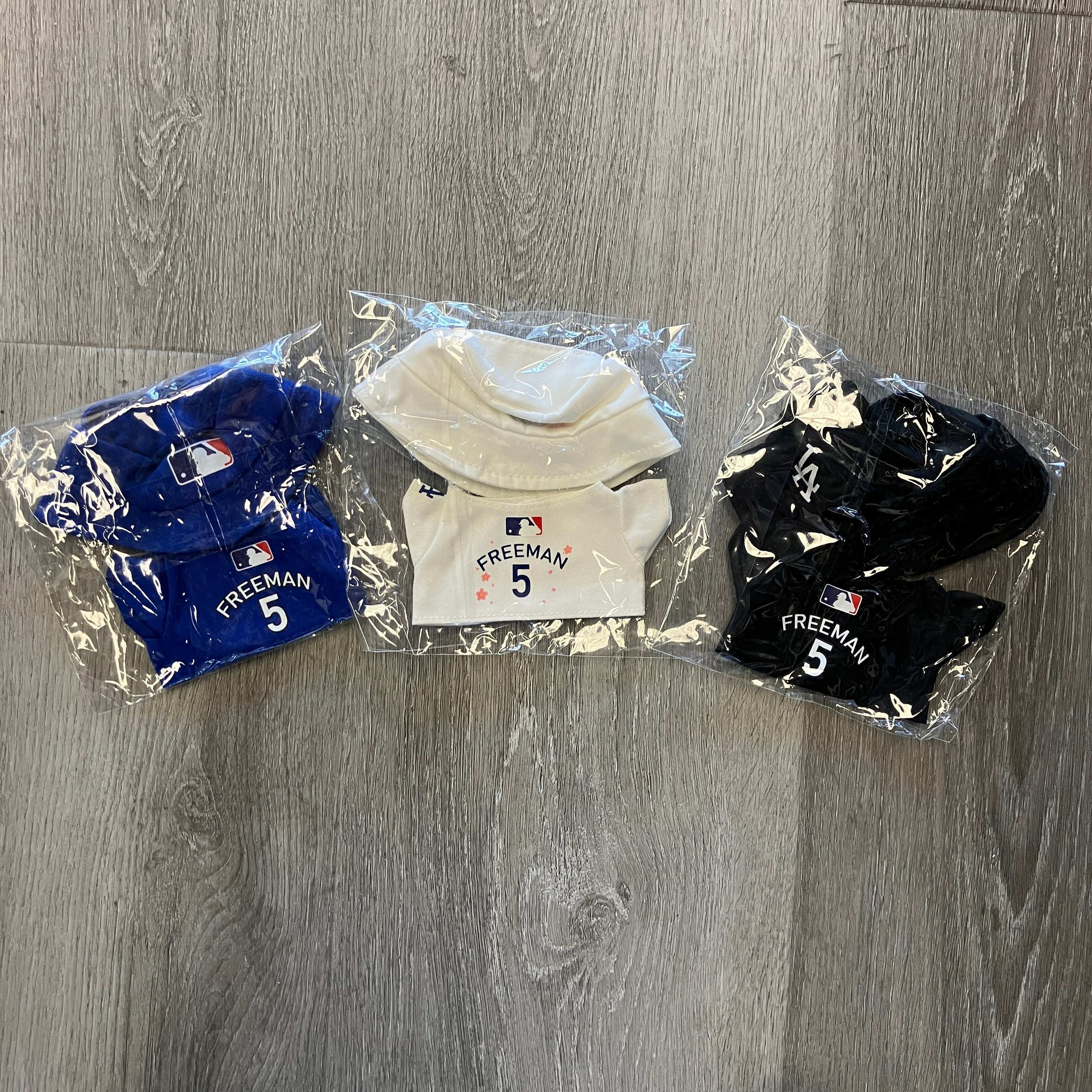 Set of black, blue, and white Freddie Freeman Labubu Dodger jerseys in packaging on wooden floor