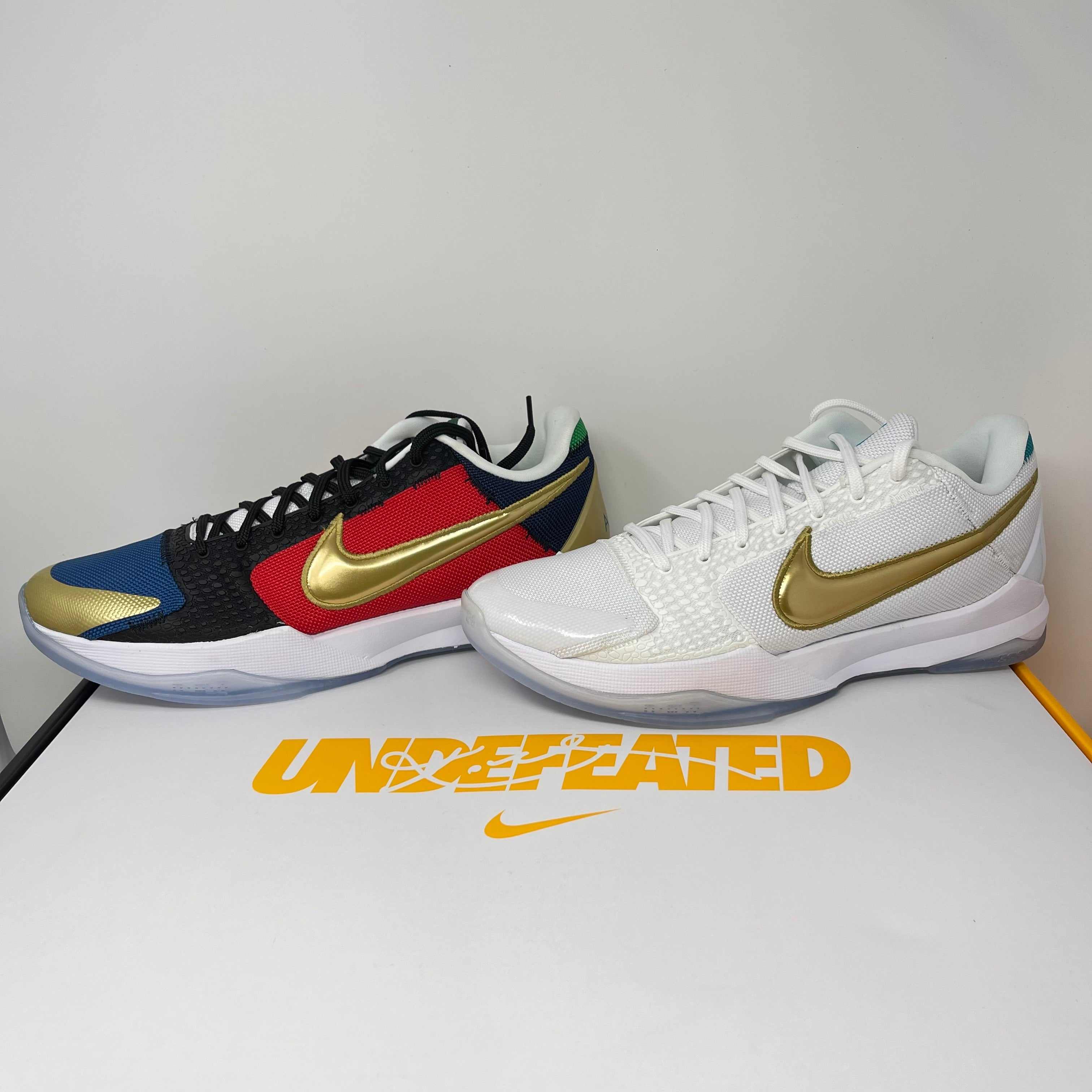 Pair of brand new Nike Kobe 5 Protro Undefeated What If Pack sneakers, one multicolor with gold swoosh and one white with gold swoosh, on Undefeated branded box