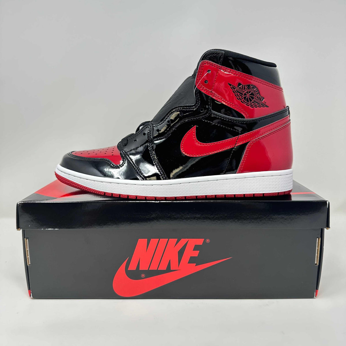 Jordan 1 Retro High OG high-top sneaker in glossy black and red patent leather, with Swoosh and white midsole.