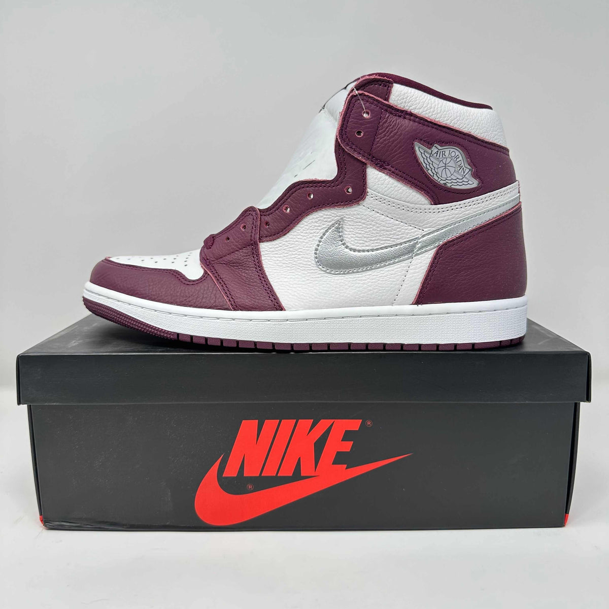 Jordan 1 Retro High OG Bordeaux sneaker in white and bordeaux leather with a silver swoosh and high-top design on a black Nike box