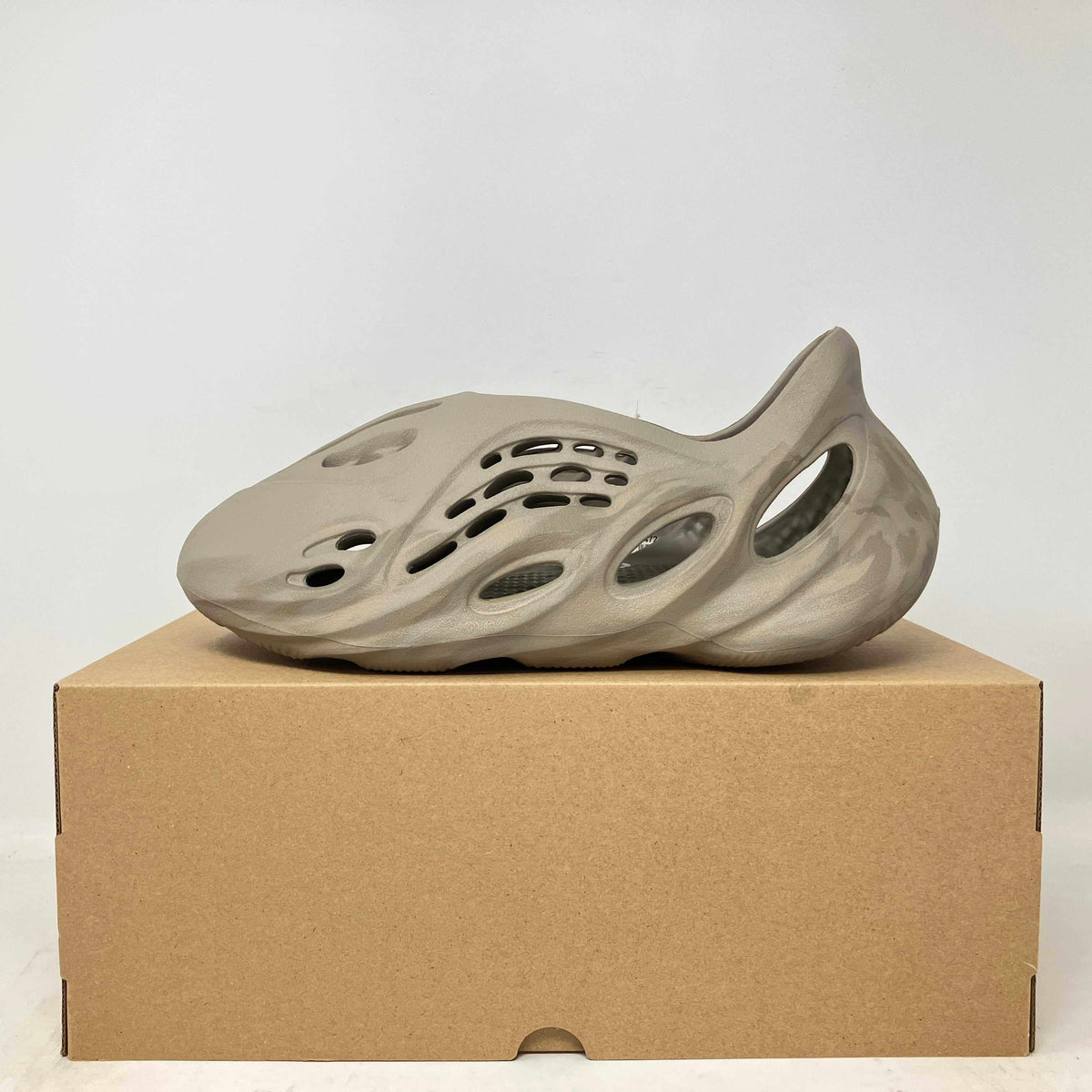 adidas Yeezy slip-on shoe in stone sage color with perforated foam design and sculpted sole sitting on a cardboard box