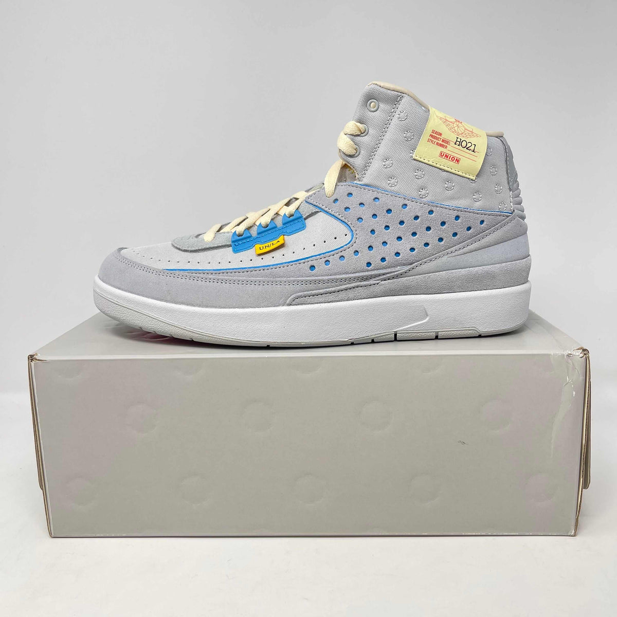Jordan 2 Retro SP sneaker in grey fog with blue accents, perforated suede upper, cream laces, and a white sole.
