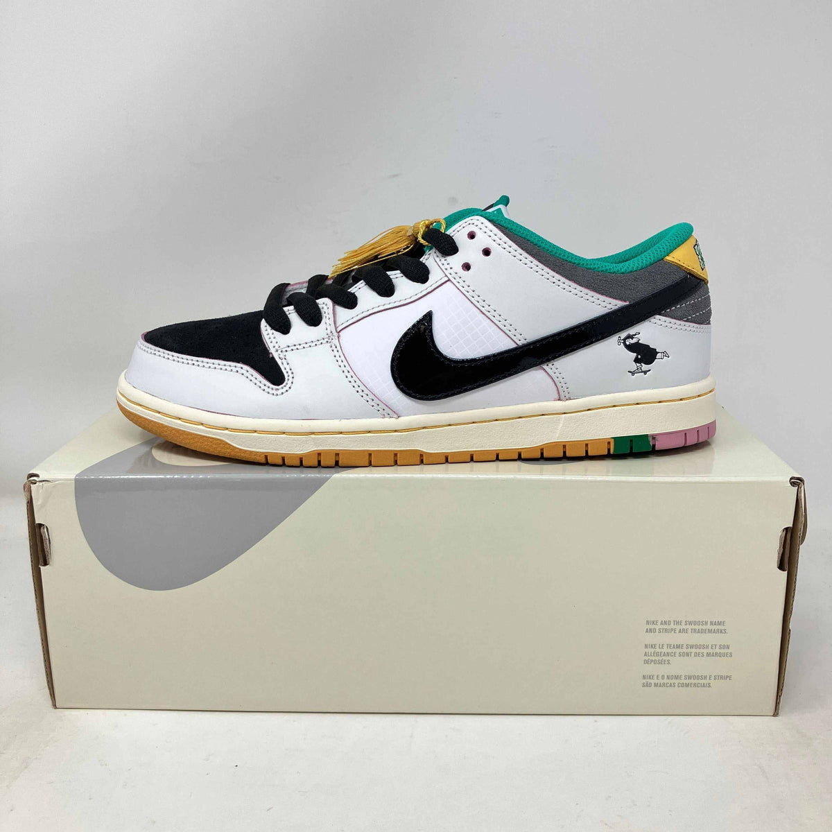 Nike SB Dunk Low sneaker in white leather with black suede toe and swoosh, teal collar, yellow accents, and multicolor outsole