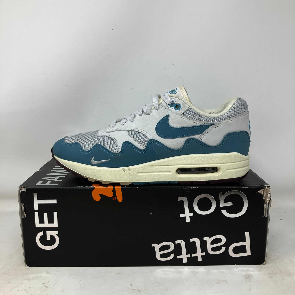 Nike Air Max 1 sneaker in white and aqua blue with wave patterns and mesh detailing on a black Patta branded box