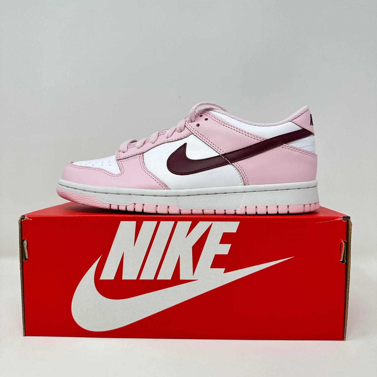 Nike Dunk Low sneaker in pink foam, white, and deep red leather with a perforated toe and classic Nike swoosh logo on side.