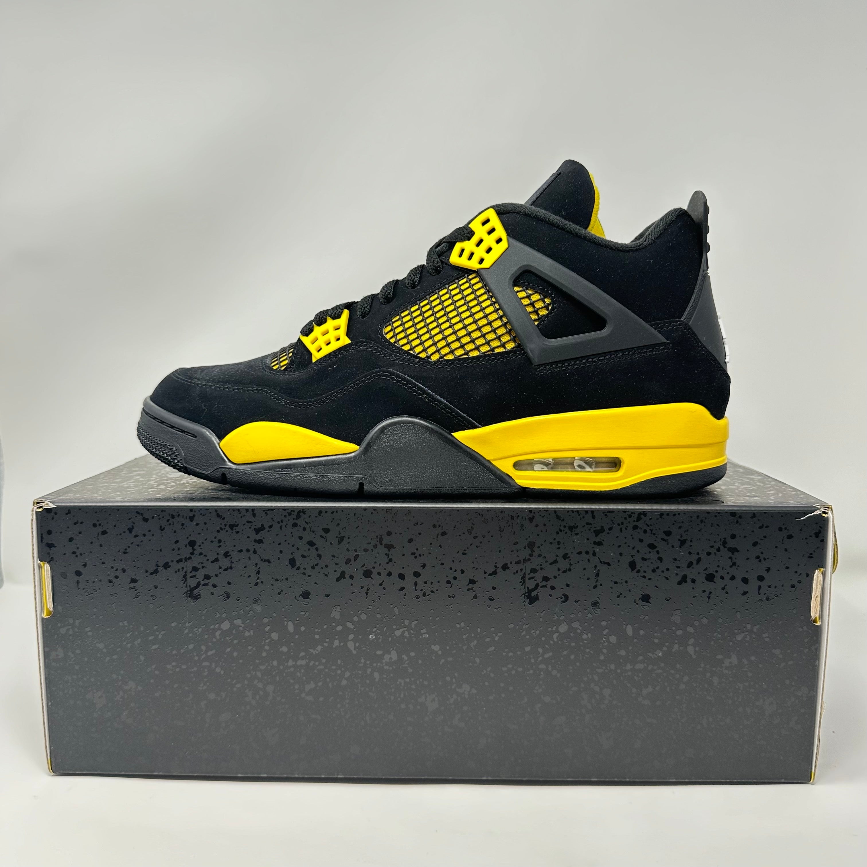 Jordan 4 Retro Thunder 2023 sneaker in black and yellow on a black speckled shoebox, brand new with accessories included.