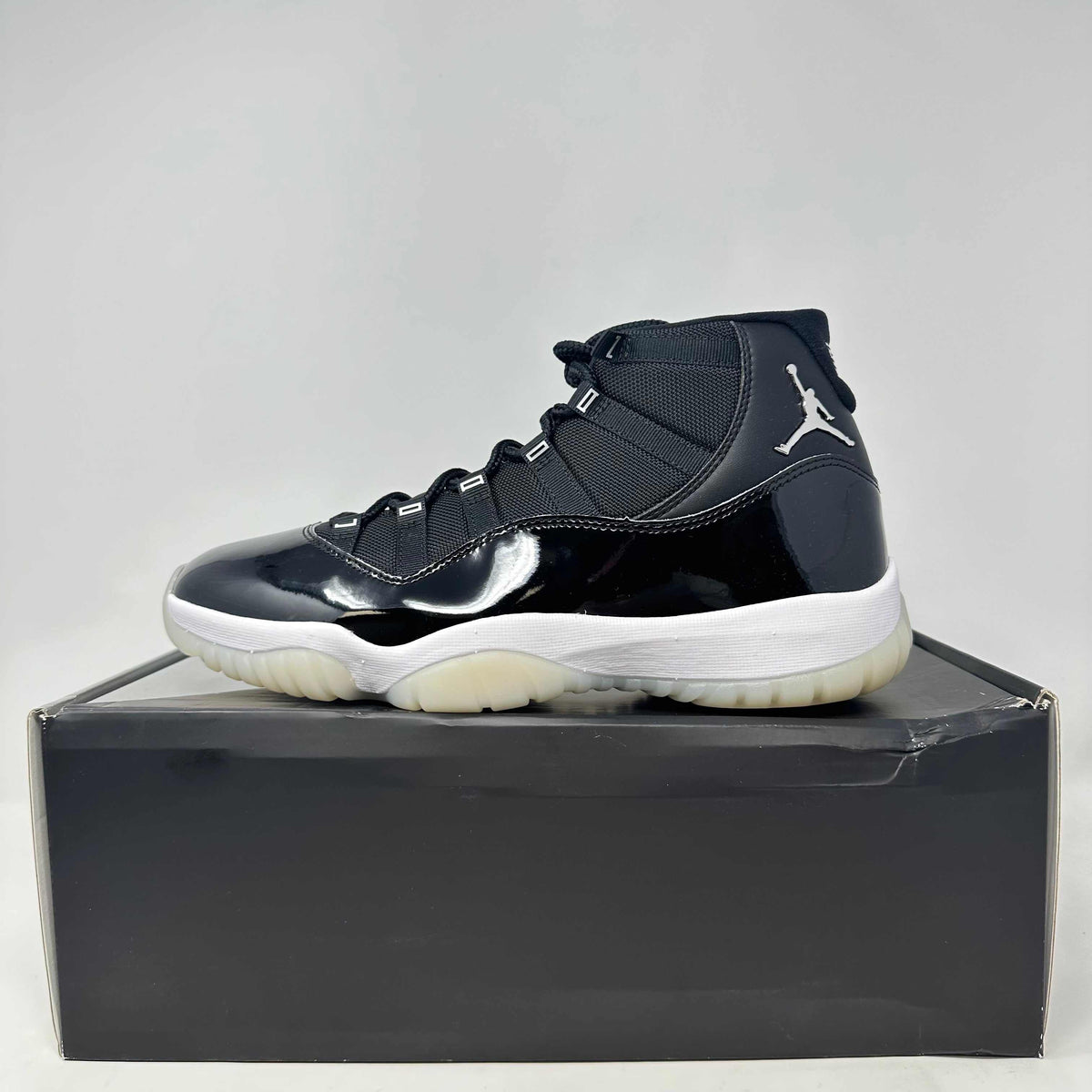 Jordan 11 Retro Jubilee black and white high-top sneaker with patent leather and mesh upper, translucent sole, and silver Jumpman logo.