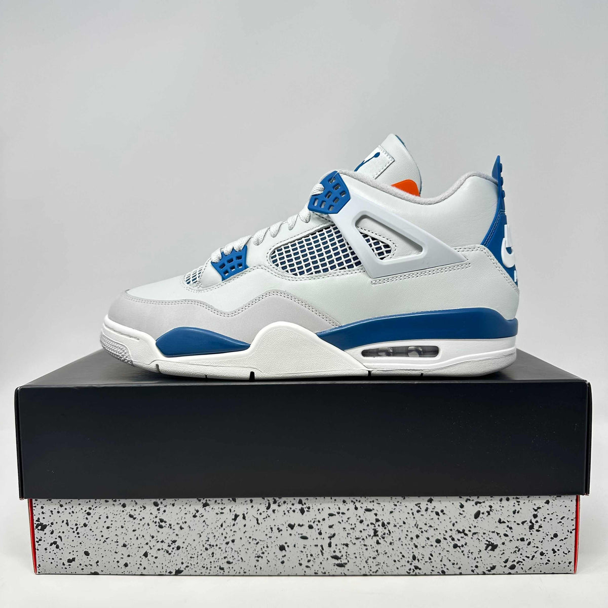 Jordan 4 Retro Military Blue sneaker in white leather with blue accents and mesh side panels on a speckled shoebox.