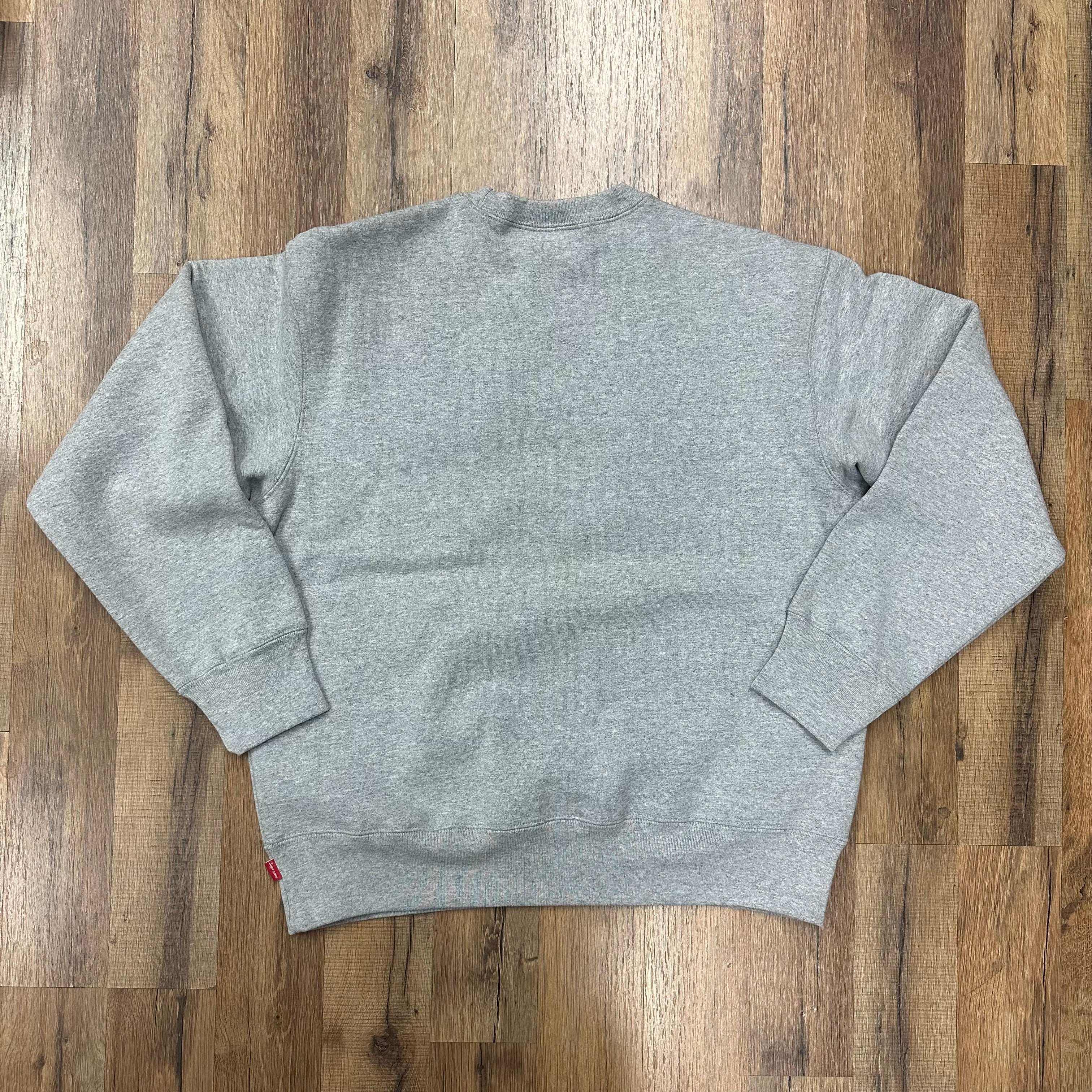 Heather grey Supreme Box Logo crewneck sweatshirt, brand new condition, on wooden floor background.