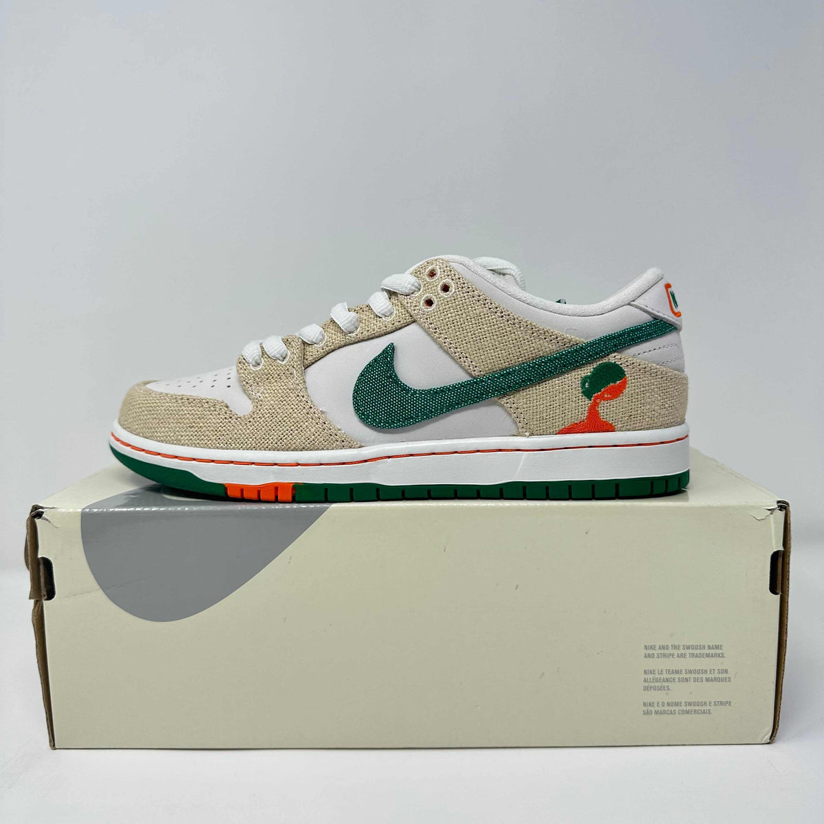 Nike SB Dunk Low sneaker in beige and white with green textured swoosh, orange sole accents, and unique orange and green logo detail