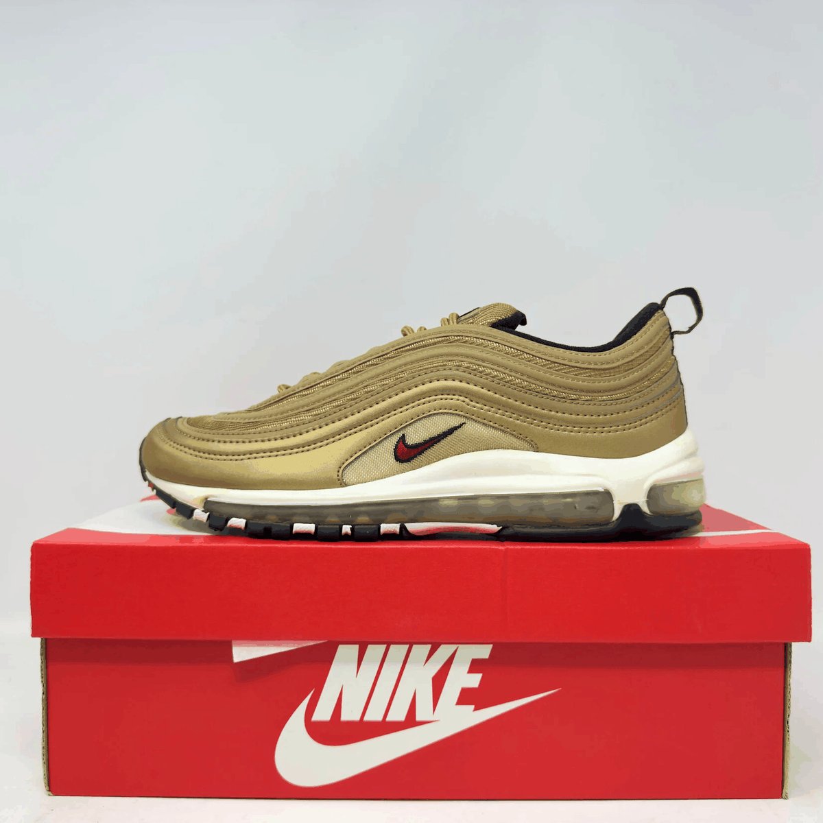 Nike Air Max 97 sneaker in metallic gold with red and black swoosh, layered upper design, and visible air sole unit.