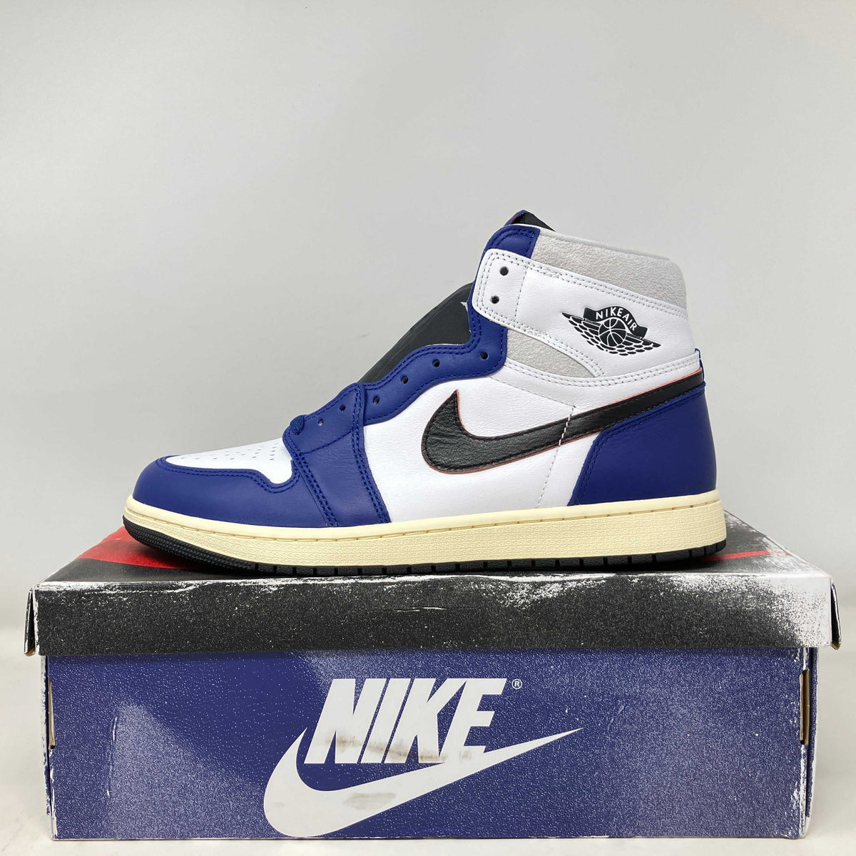 Jordan 1 Retro High OG sneaker in white, blue, black leather with cream sole and Nike wing logo on ankle panel.