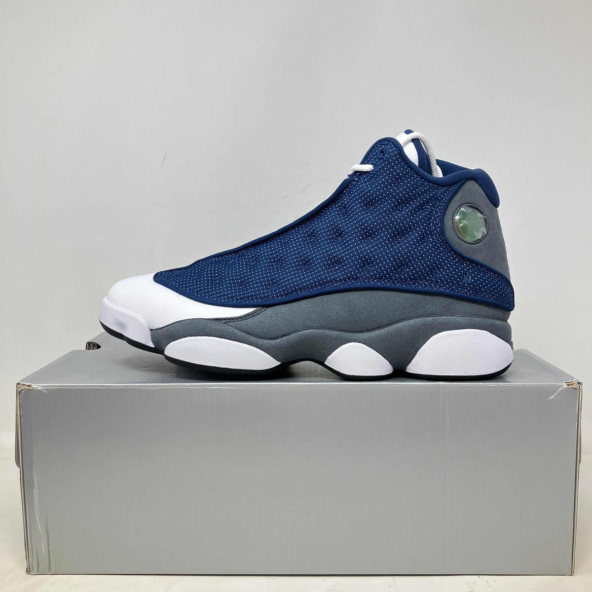 Jordan 13 Retro Flint basketball shoe in navy blue, grey suede, and white leather with a translucent side emblem and patterned sole