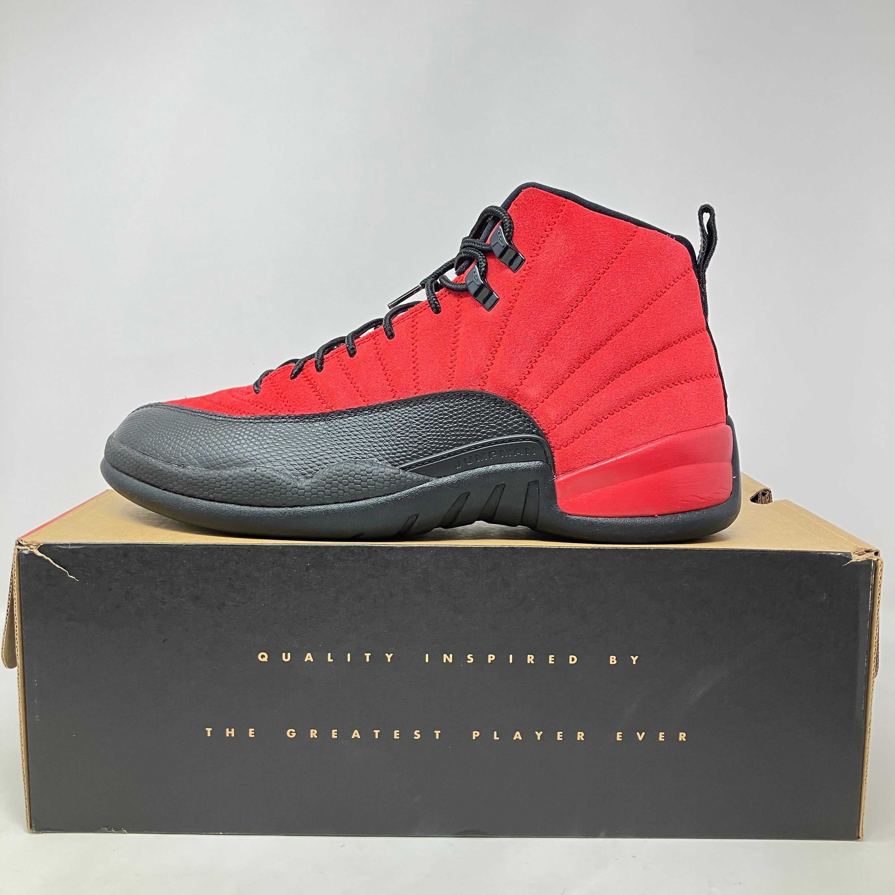 Red and black Jordan 12 Retro Reverse Flu Game sneaker on a black and brown box with gold text