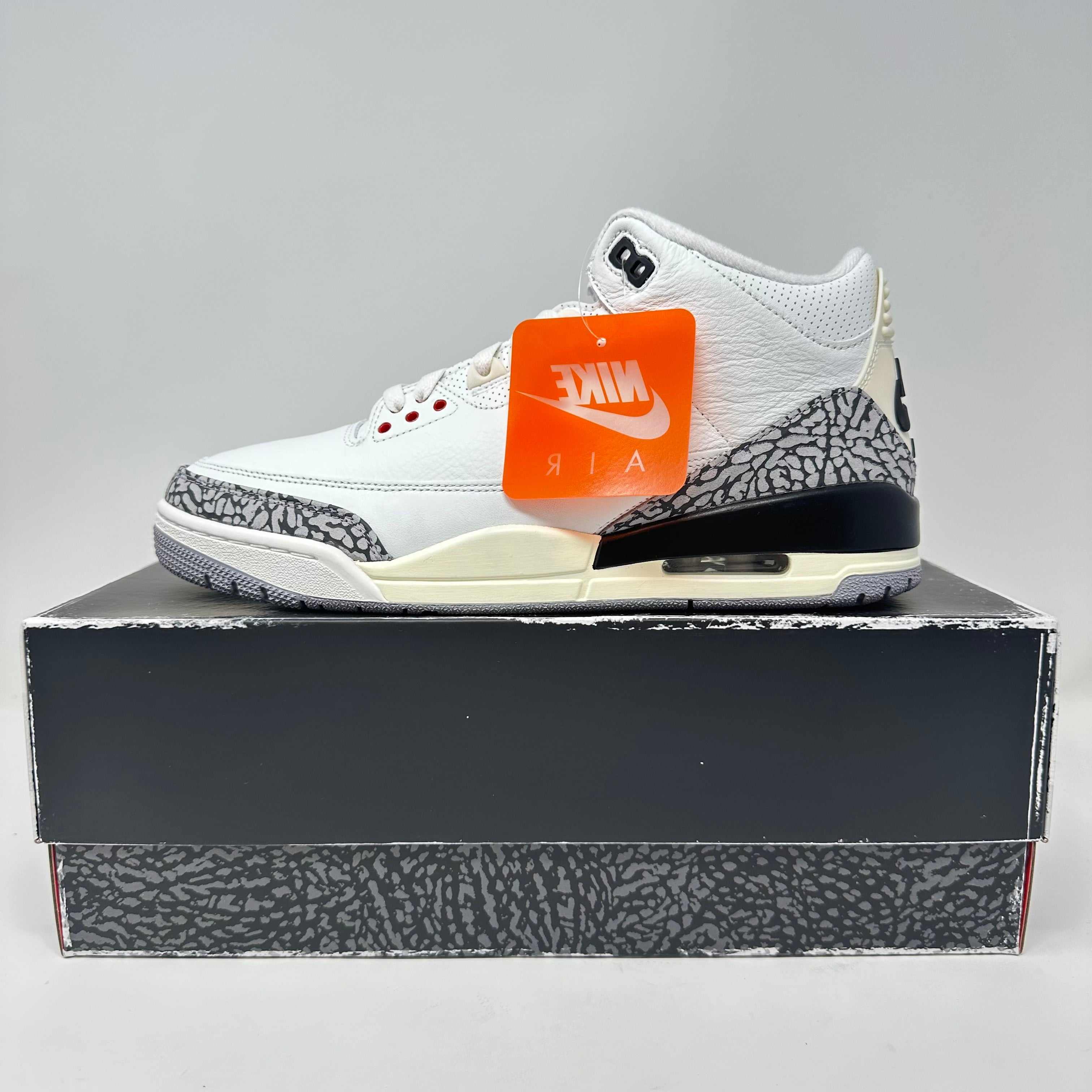 White Jordan 3 Retro sneaker with cement print on a matching box and Nike Air tag