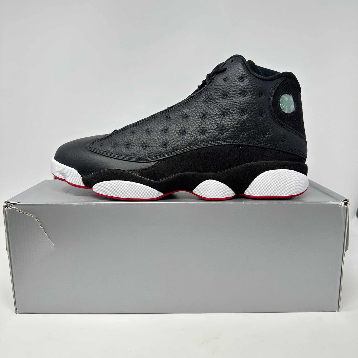 Jordan 13 Retro basketball shoe in black leather with white and red rubber sole and holographic logo on the ankle collar.