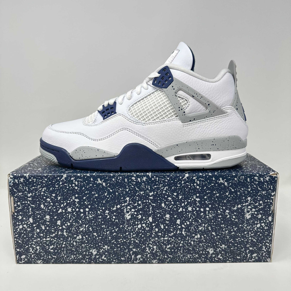 Jordan 4 Retro sneaker in white leather with navy and grey speckled accents and mesh side panels on a speckled navy box
