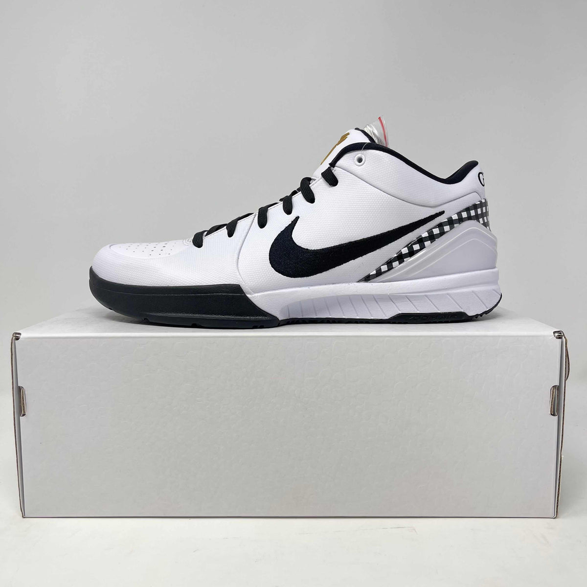 Nike Kobe 4 Protro basketball shoe in white with black leather accents, a bold swoosh, and checkered heel trim.