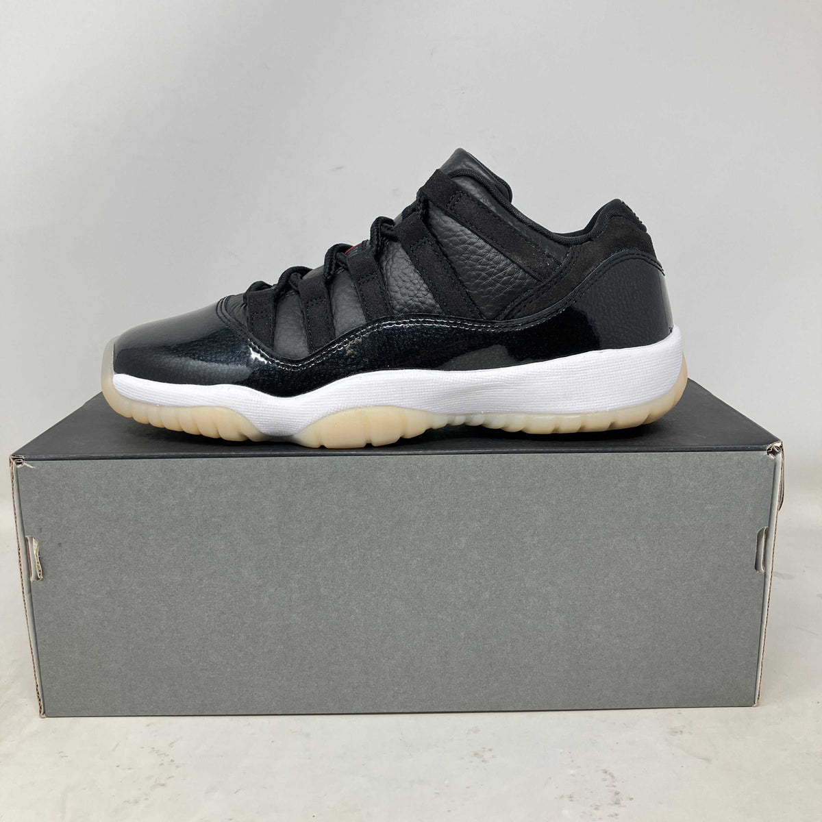 Jordan 11 Retro Low sneaker in black leather and mesh, with glossy patent panels, a white midsole, and translucent outsole.