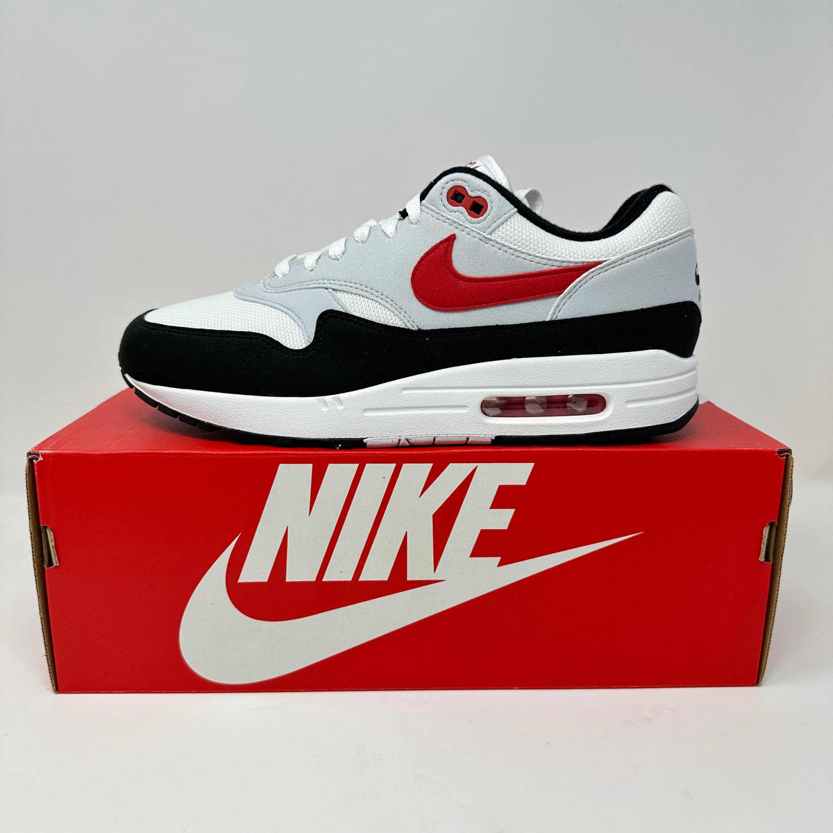 Nike Air Max 1 sneaker in white, black, and red with mesh and suede materials, featuring a visible Air Max cushioning unit.
