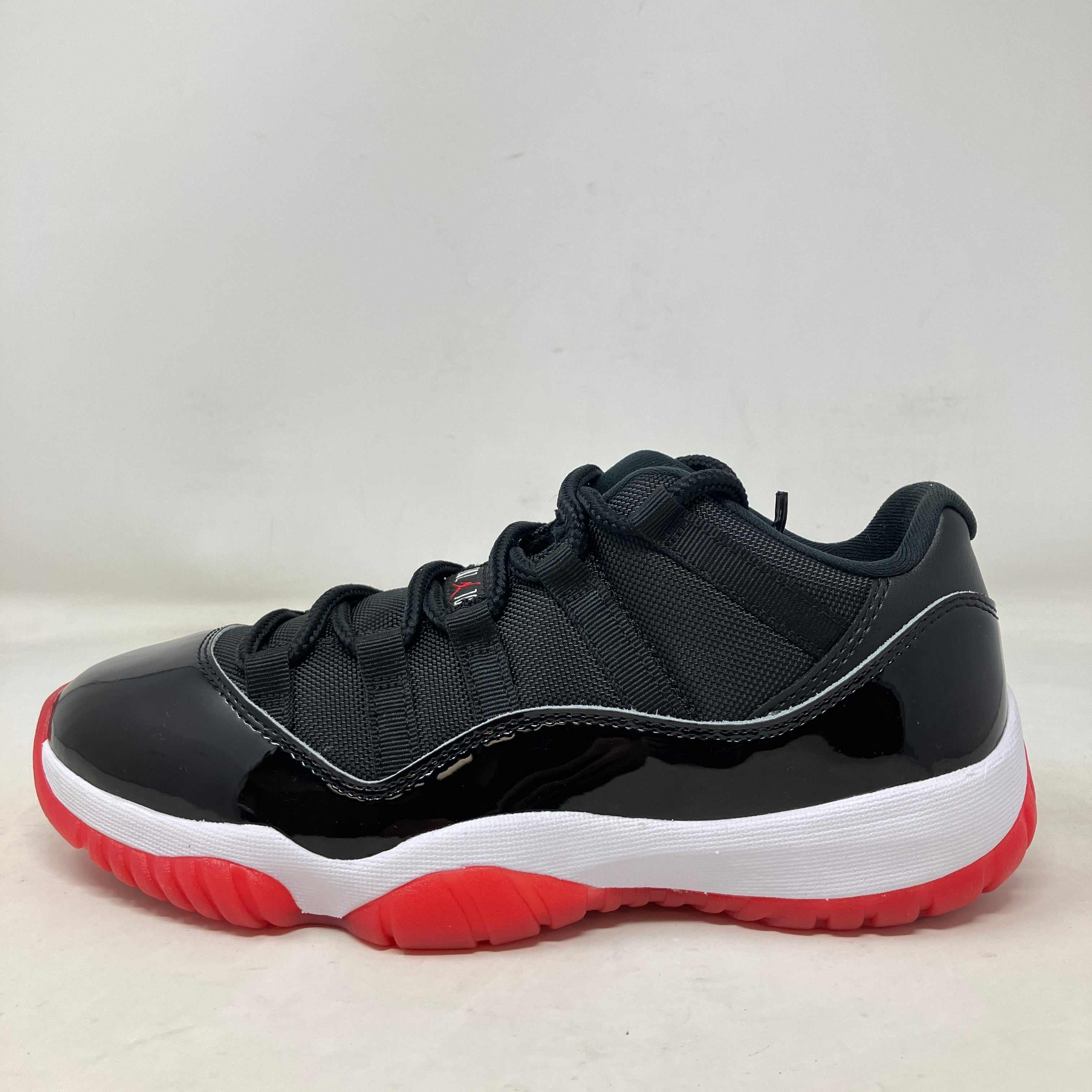 Jordan 11 Retro Low Bred sneaker in black patent leather with red outsole and white midsole, brand new without box