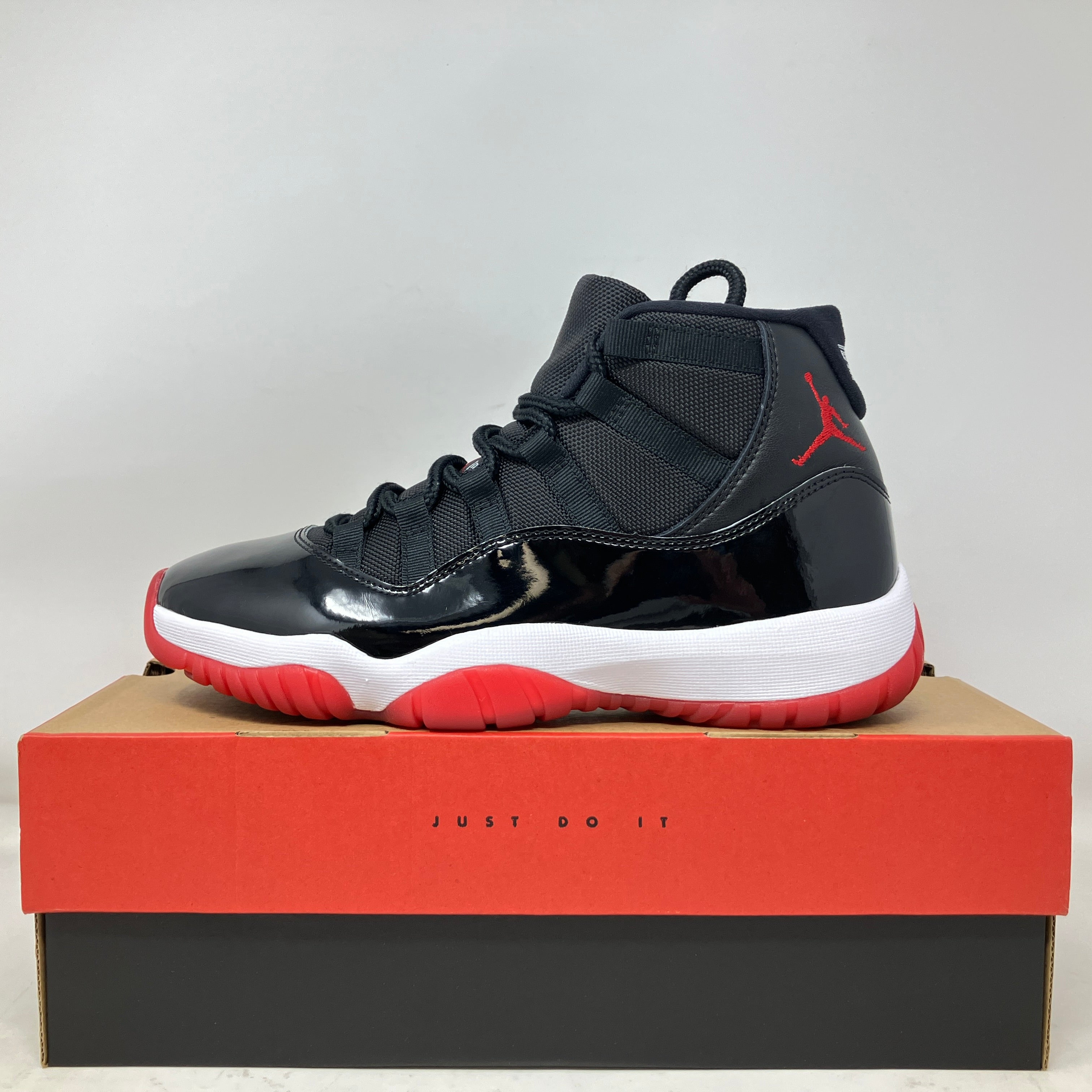 Black and red Jordan 11 Retro Playoffs Bred sneaker on box with Nike "Just Do It" slogan