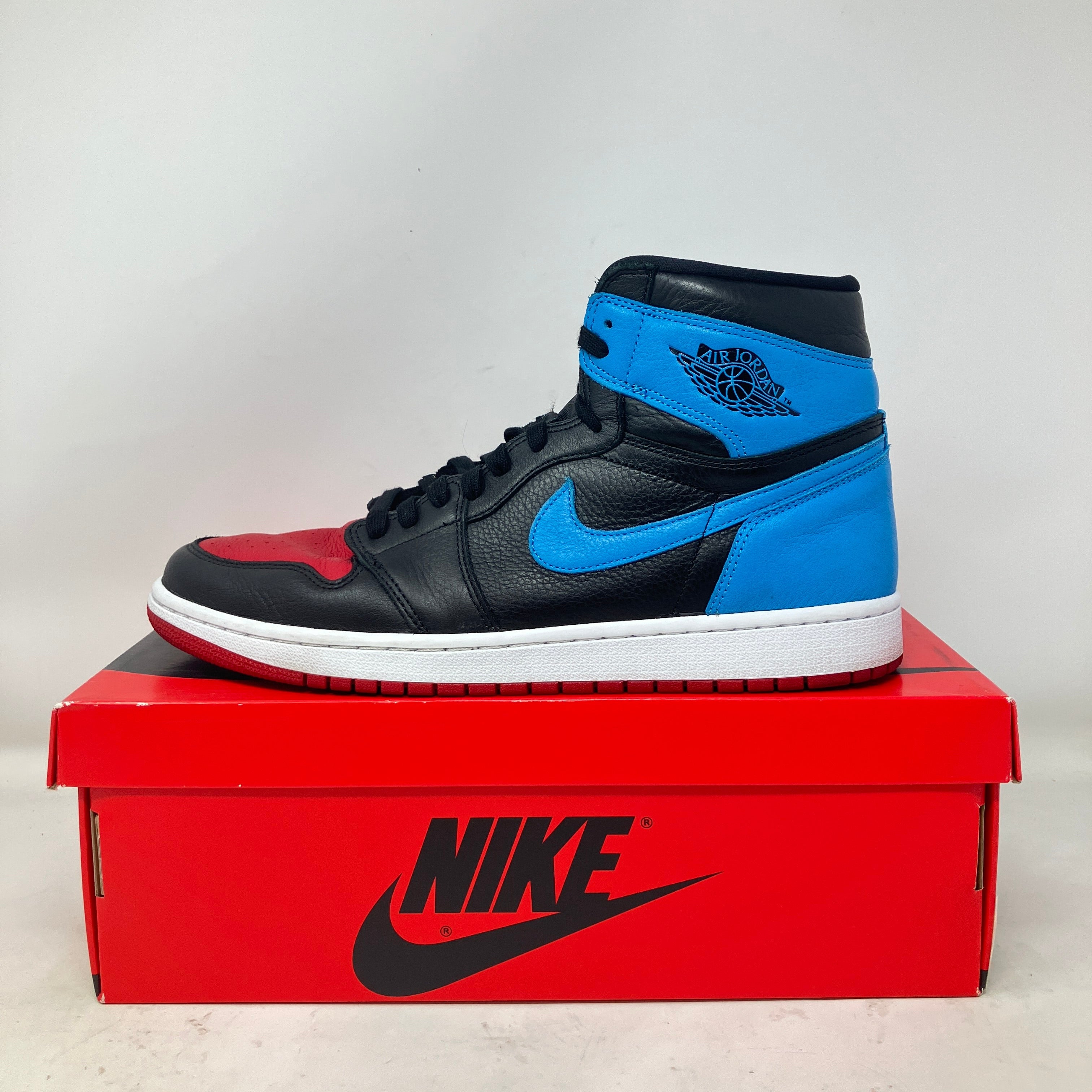 Jordan 1 Retro High women's sneaker in black, red, and blue, pre-owned with accessories on red Nike box