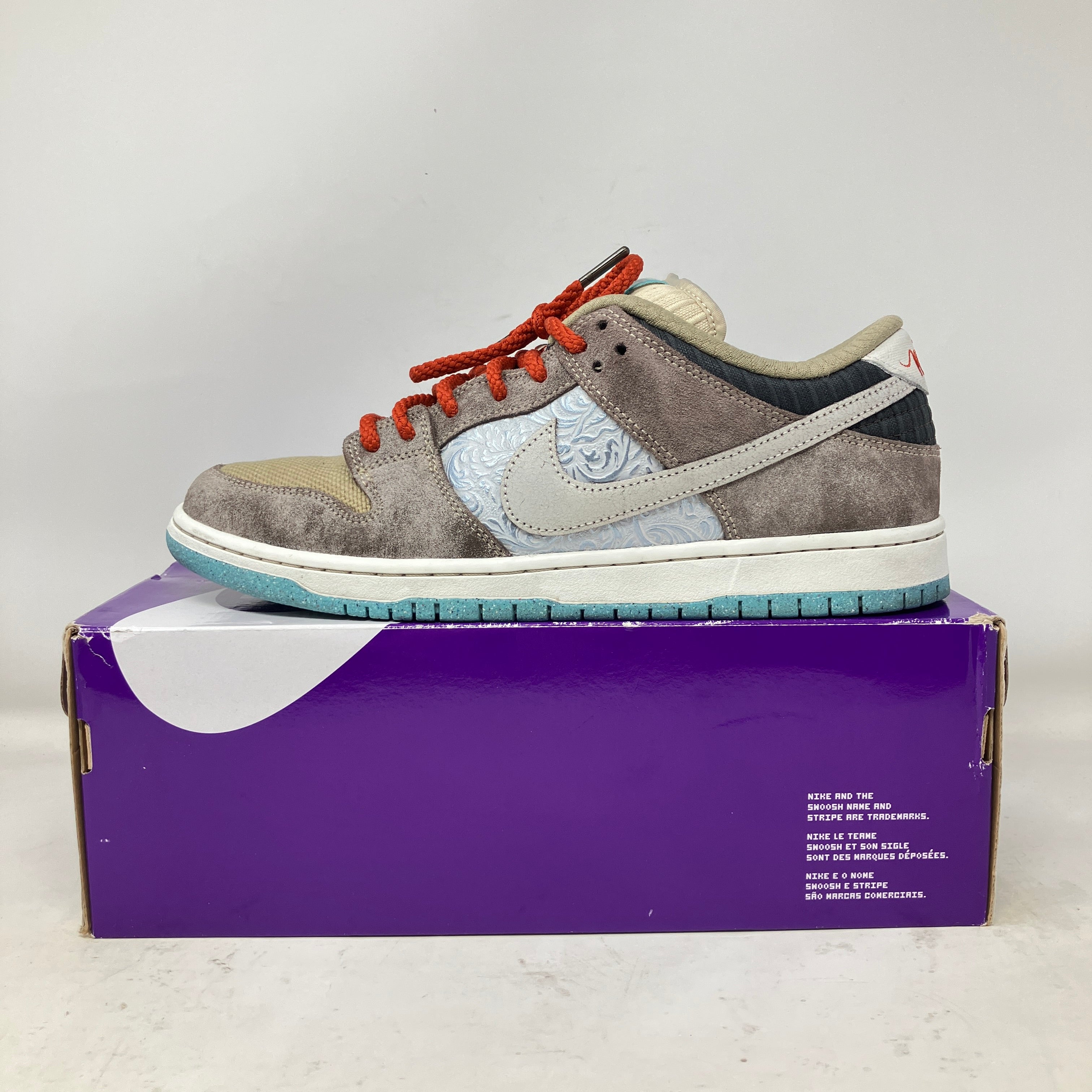 Nike SB Dunk Low sneaker in mixed suede and leather with light blue sole on purple box, pre-owned condition with accessories and replacement box label.