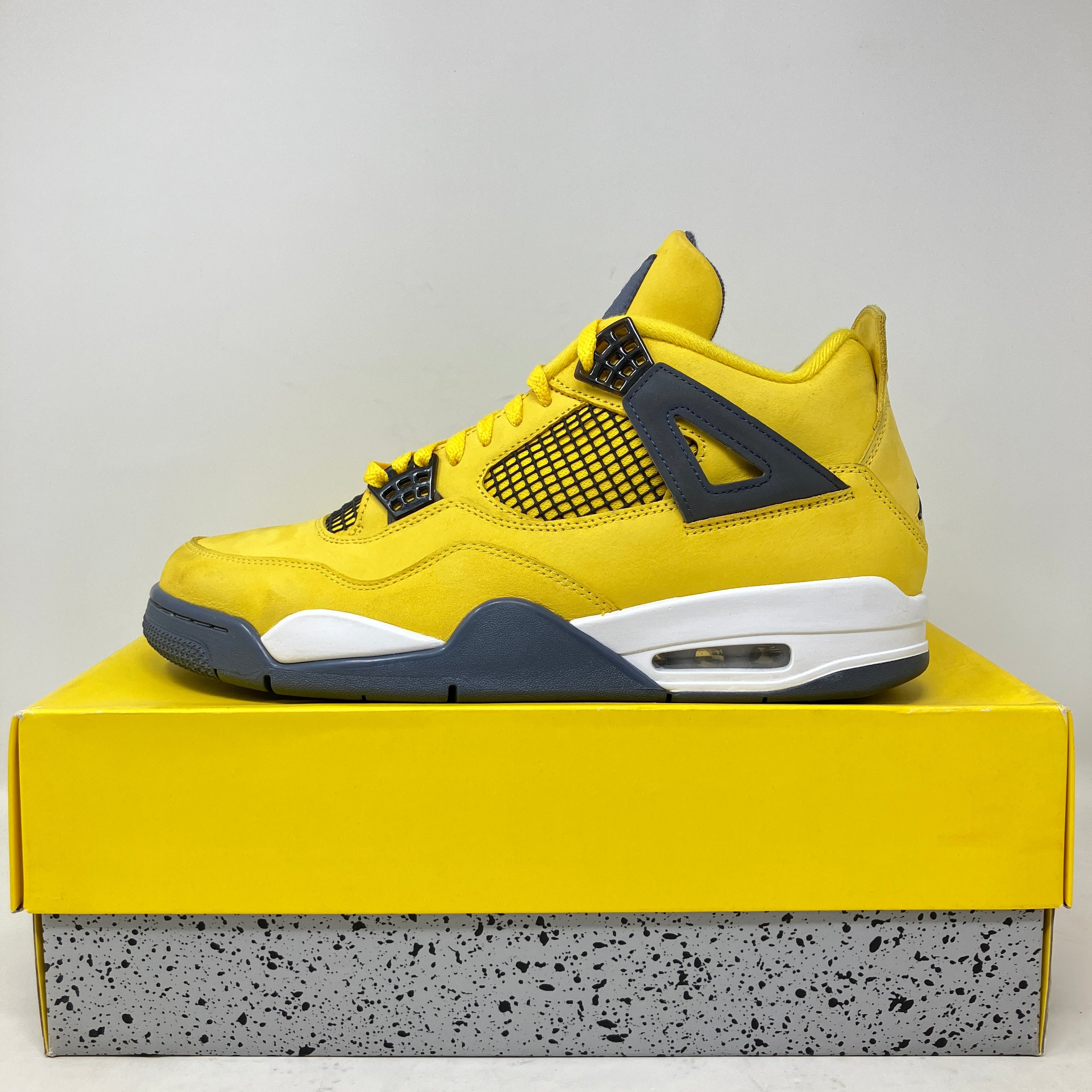 Jordan 4 Retro Lightning 2021 yellow and black sneaker on yellow and speckled shoebox, pre-owned with all accessories included.