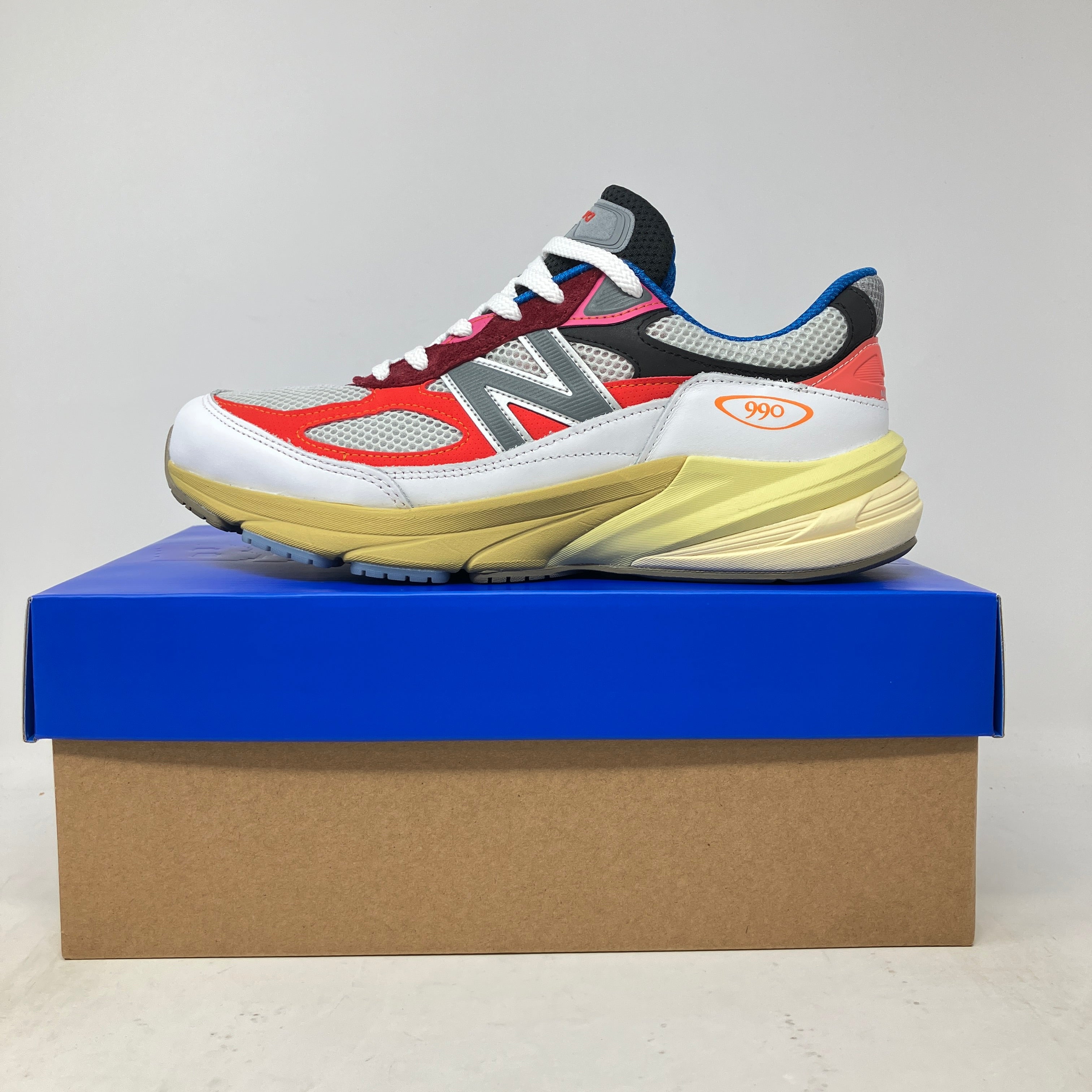 New Balance 990v6 MiUSA Action Bronson sneaker in red, gray, and yellow on a blue and brown shoebox